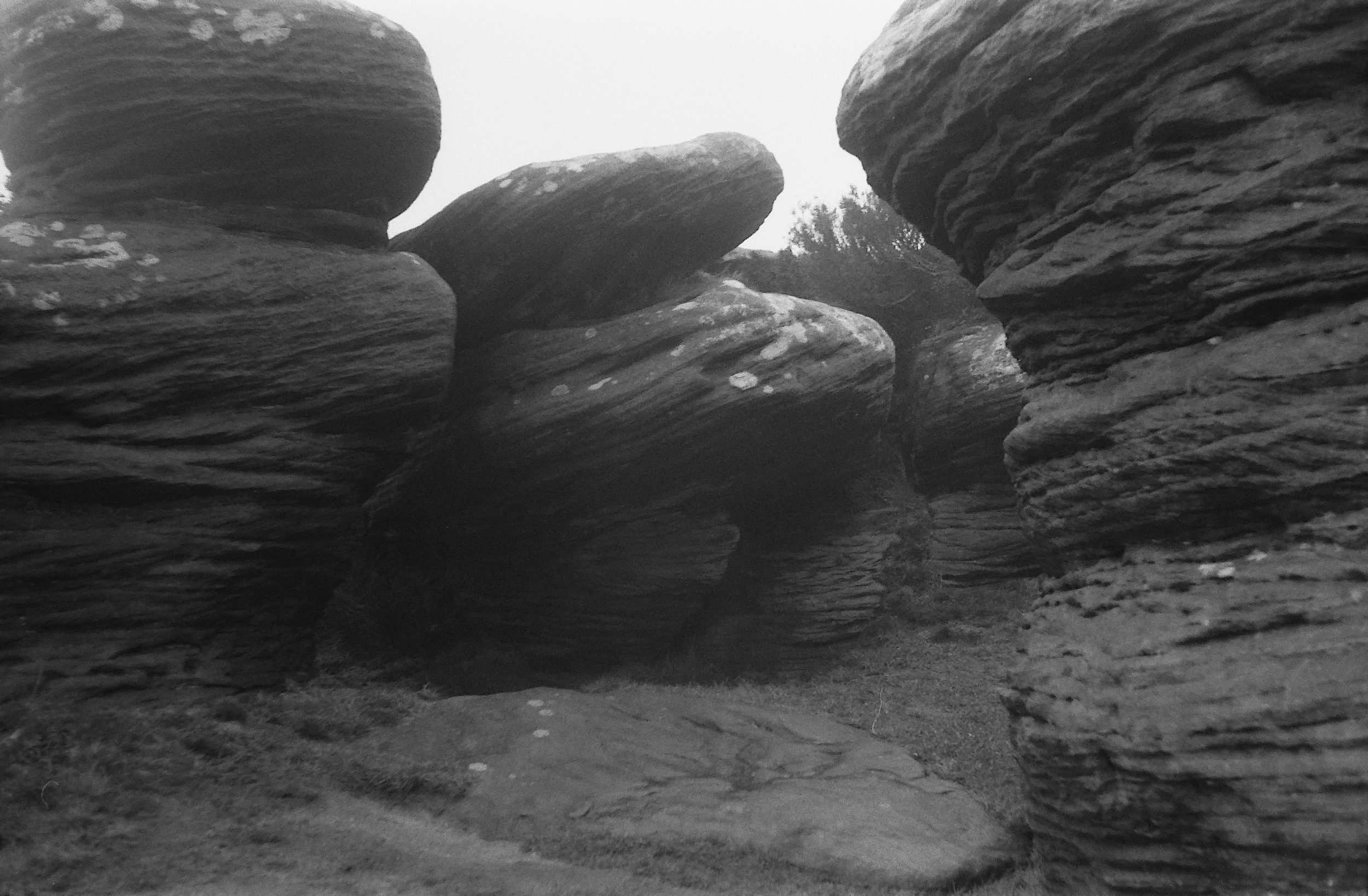 Black and white photo of layered rock formations with a cloudy sky in the background.