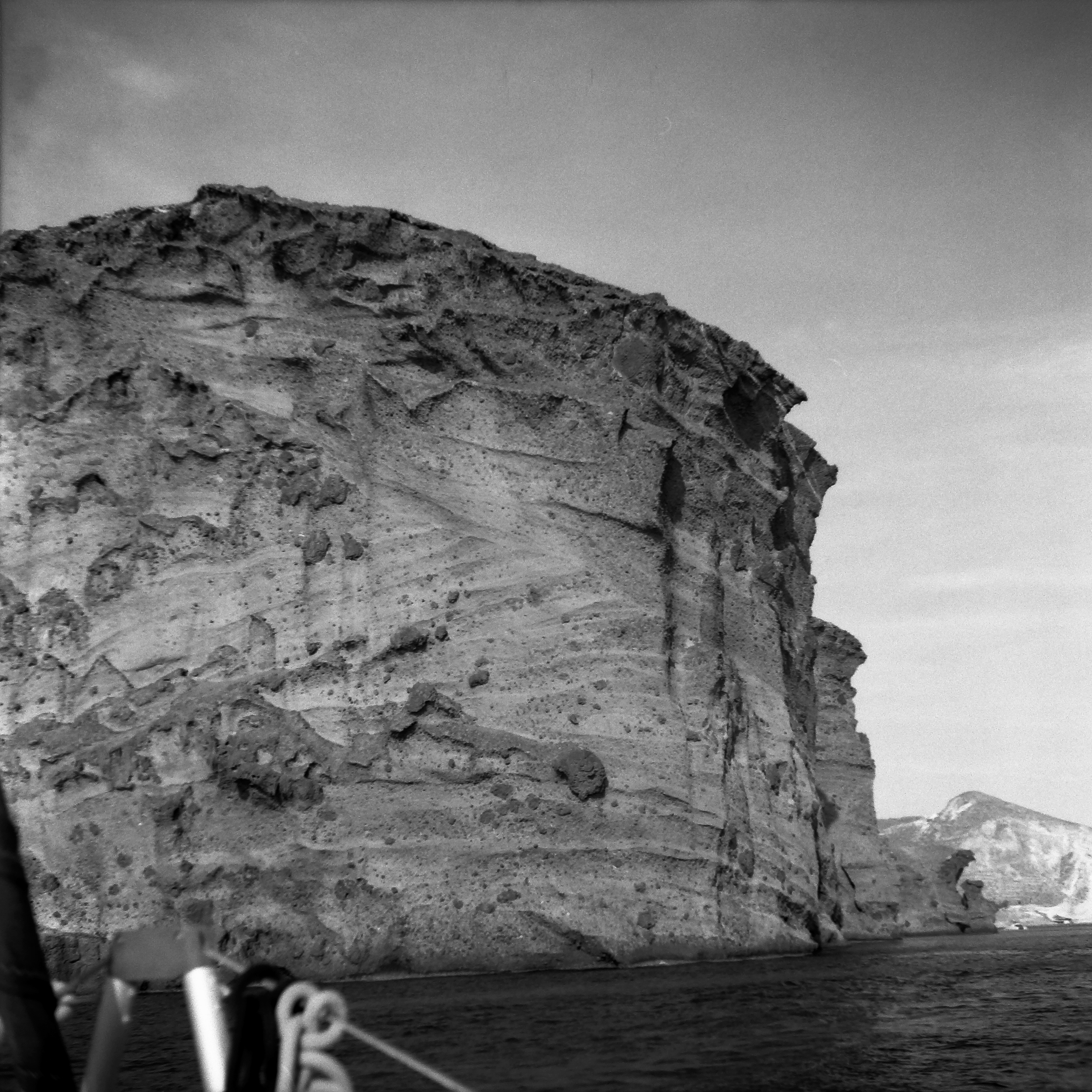 Close-up view of a rocky and sandy cliff or mountain with a clear sky in the background, black and white photograph.