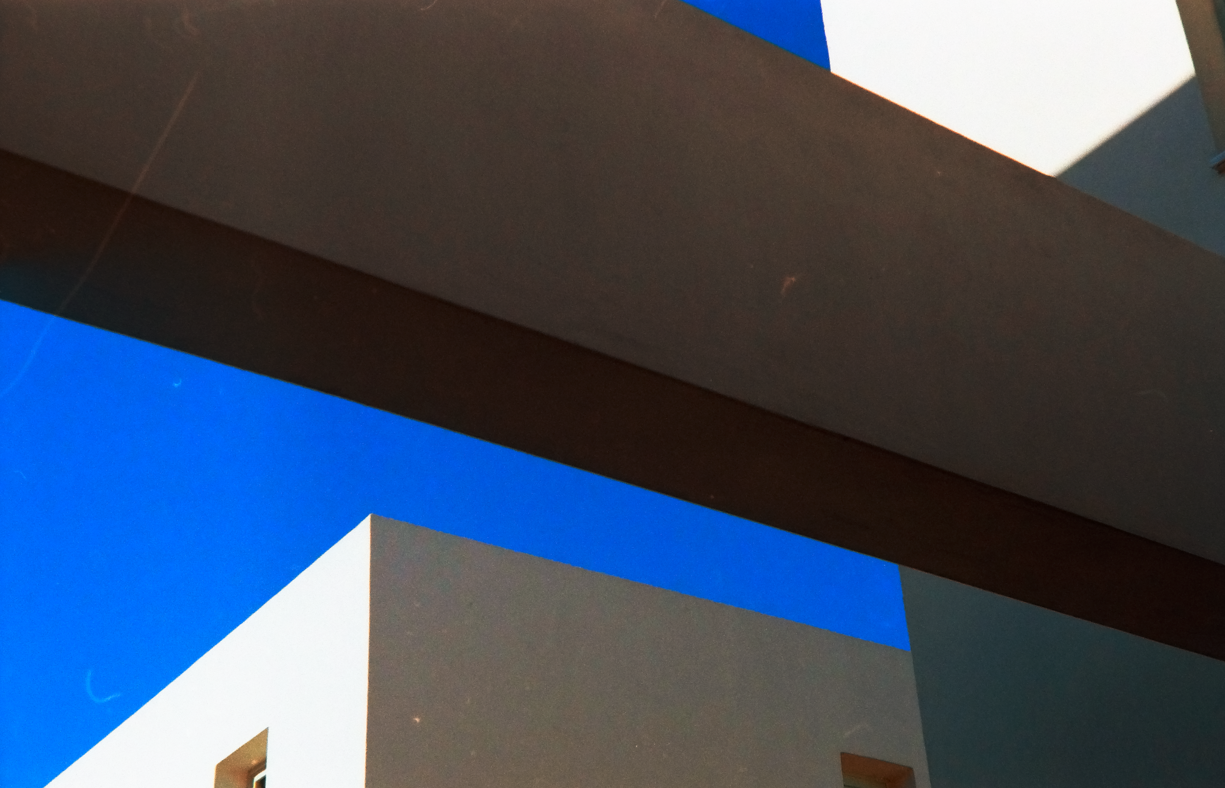 Close-up view of a modern architectural structure with geometric shapes and clean lines against a clear blue sky, featuring dark gray, white, and blue panels.