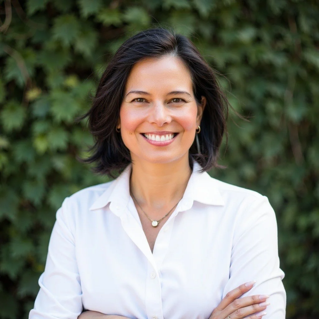 Laveena Archers 3/5 Human Design Projector Teacher Smiling with dark hair in a white shirt against a foliage background.
