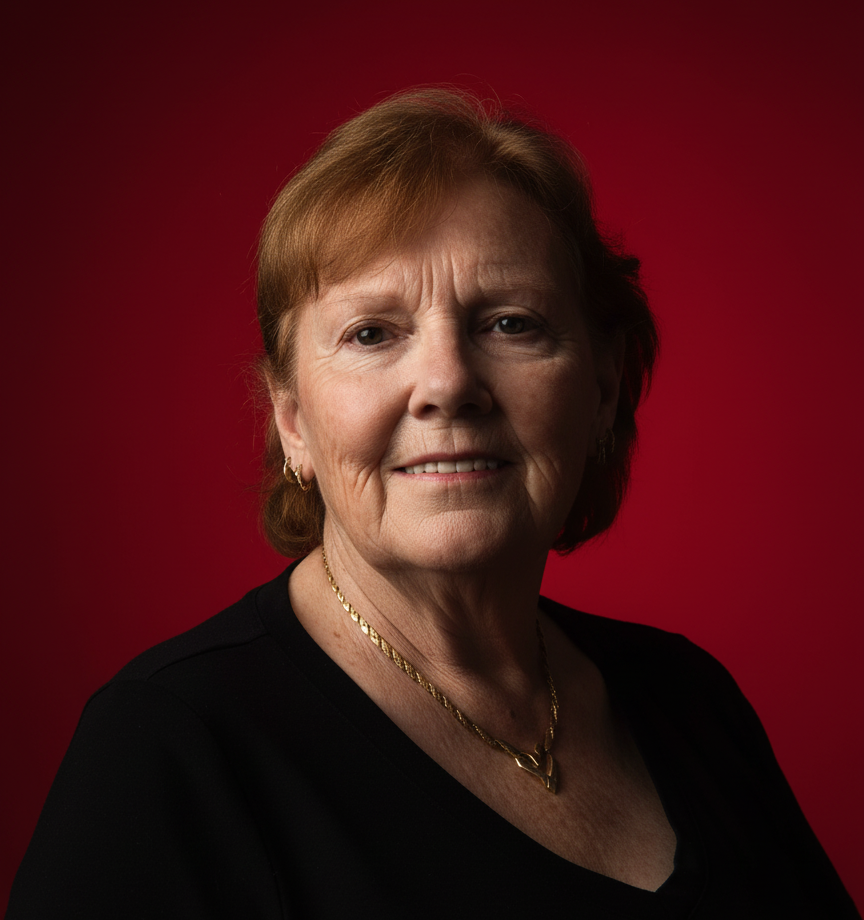 A portrait of an elderly woman with short, light brown hair, wearing a black top and gold jewelry, against a red backdrop.