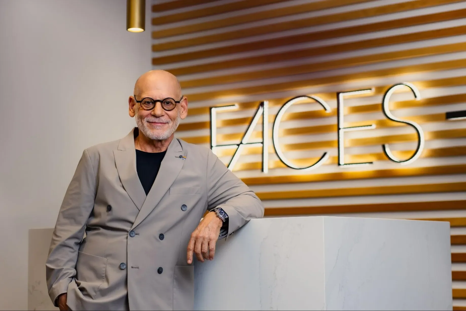 Image of a plastic suregeon in front of hospitality sytle reception desk and brand wall.