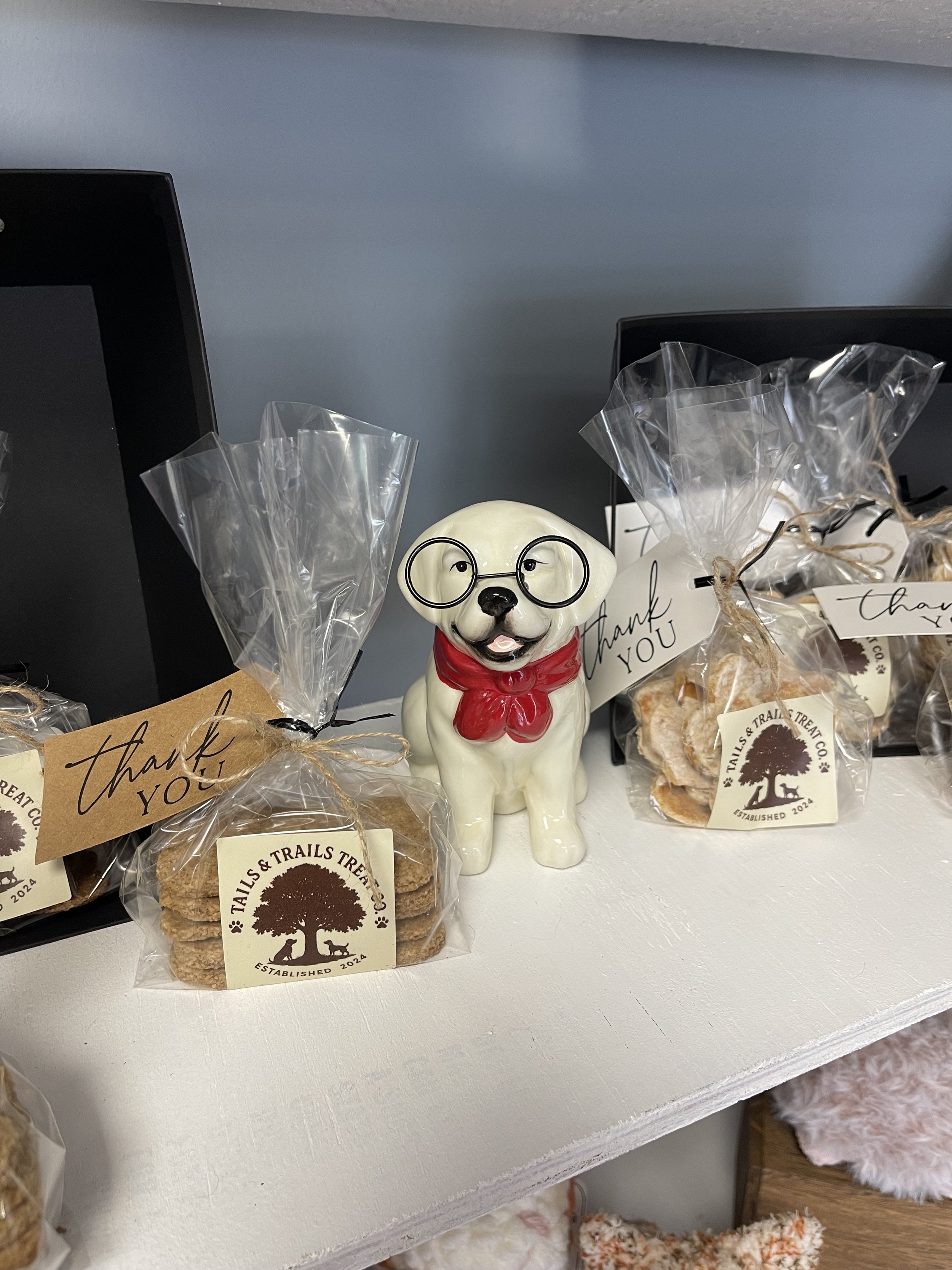 Image of a dog statue sitting on a shelf flanked by treats baked by Tails & Trails Treat Co.