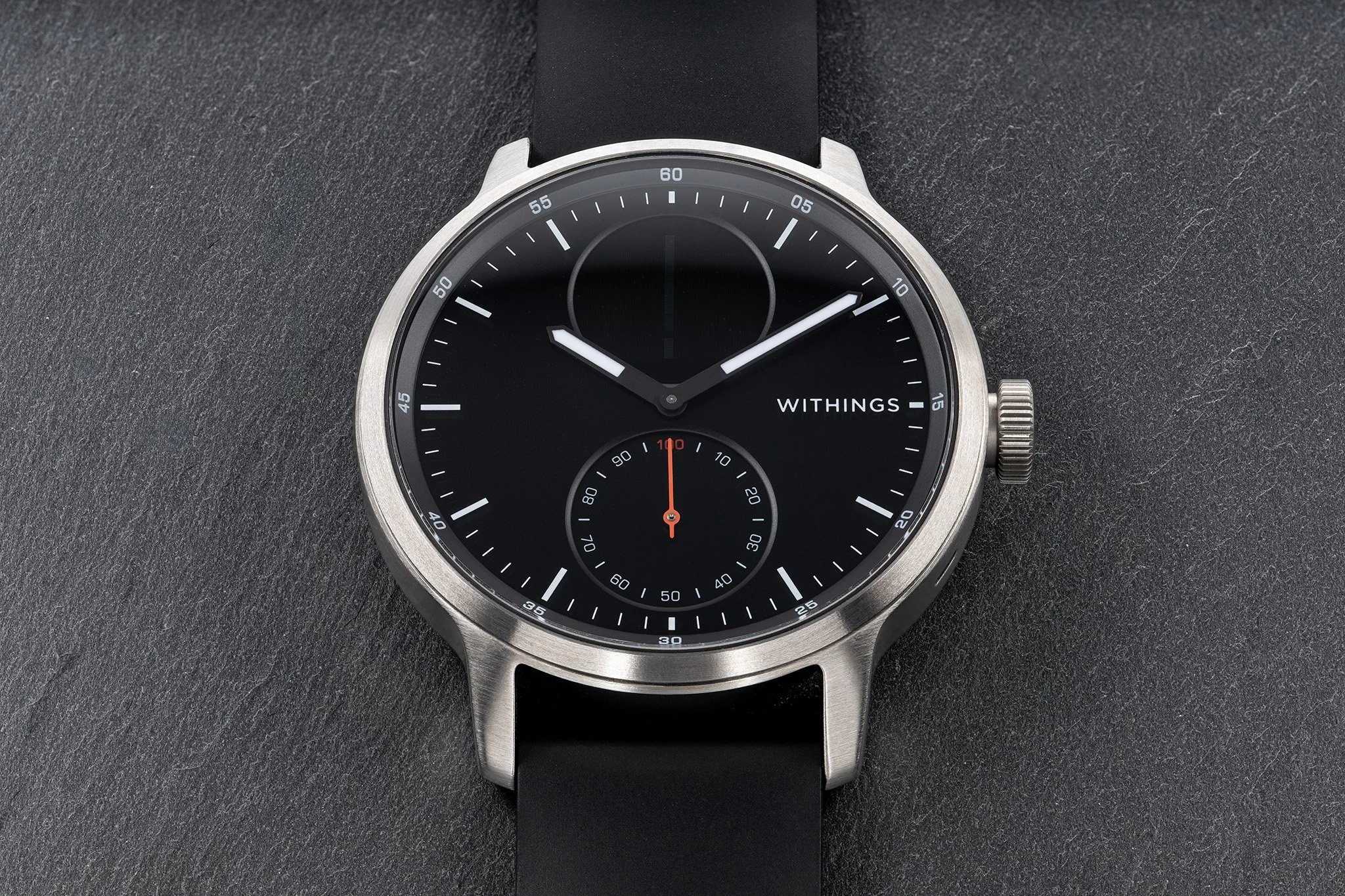 Professionelle Produktfotografie Withings Smartwatch, Draufsicht auf schwarzem Schieferhintergrund, Fokus auf gebürstetem Edelstahlgehäuse und Zifferblatt-Details, technischer Clean-Shot.