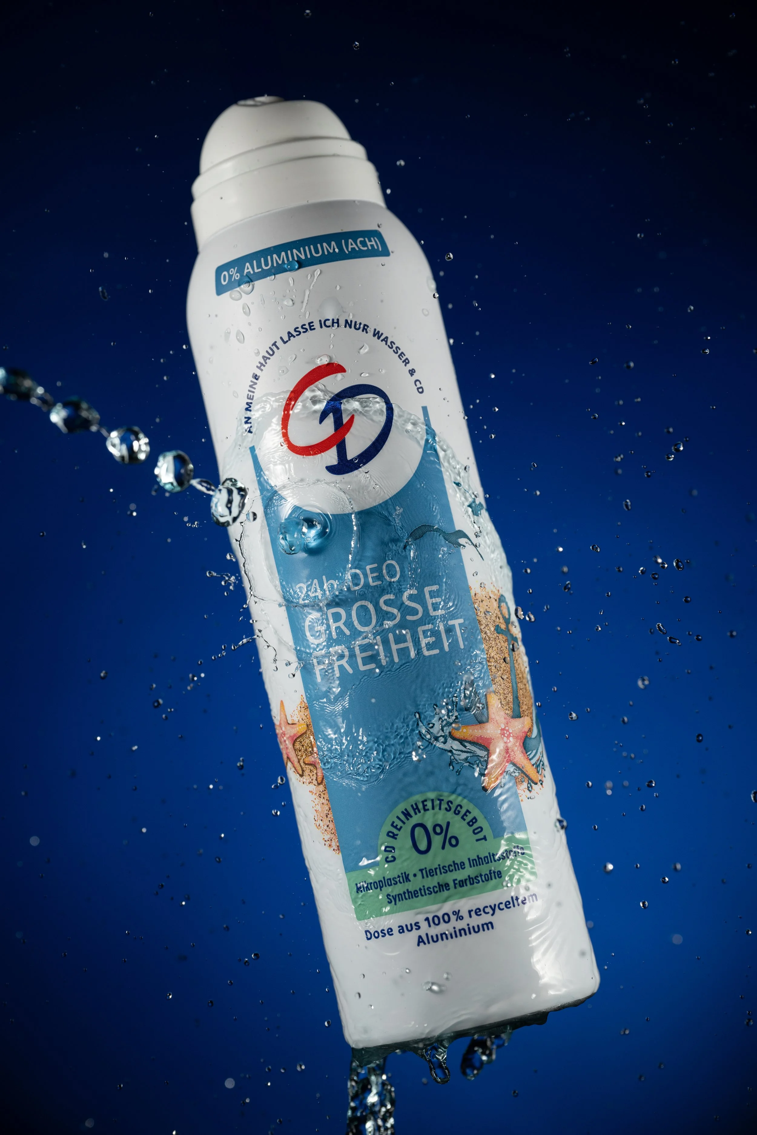 Professionelle Produktfotografie CD Deo Spray "Grosse Freiheit", dynamische Inszenierung mit Wasser-Splash und Tropfenkette vor tiefblauem Hintergrund, Fokus auf maritime Gestaltungselemente, technischer Clean-Shot.