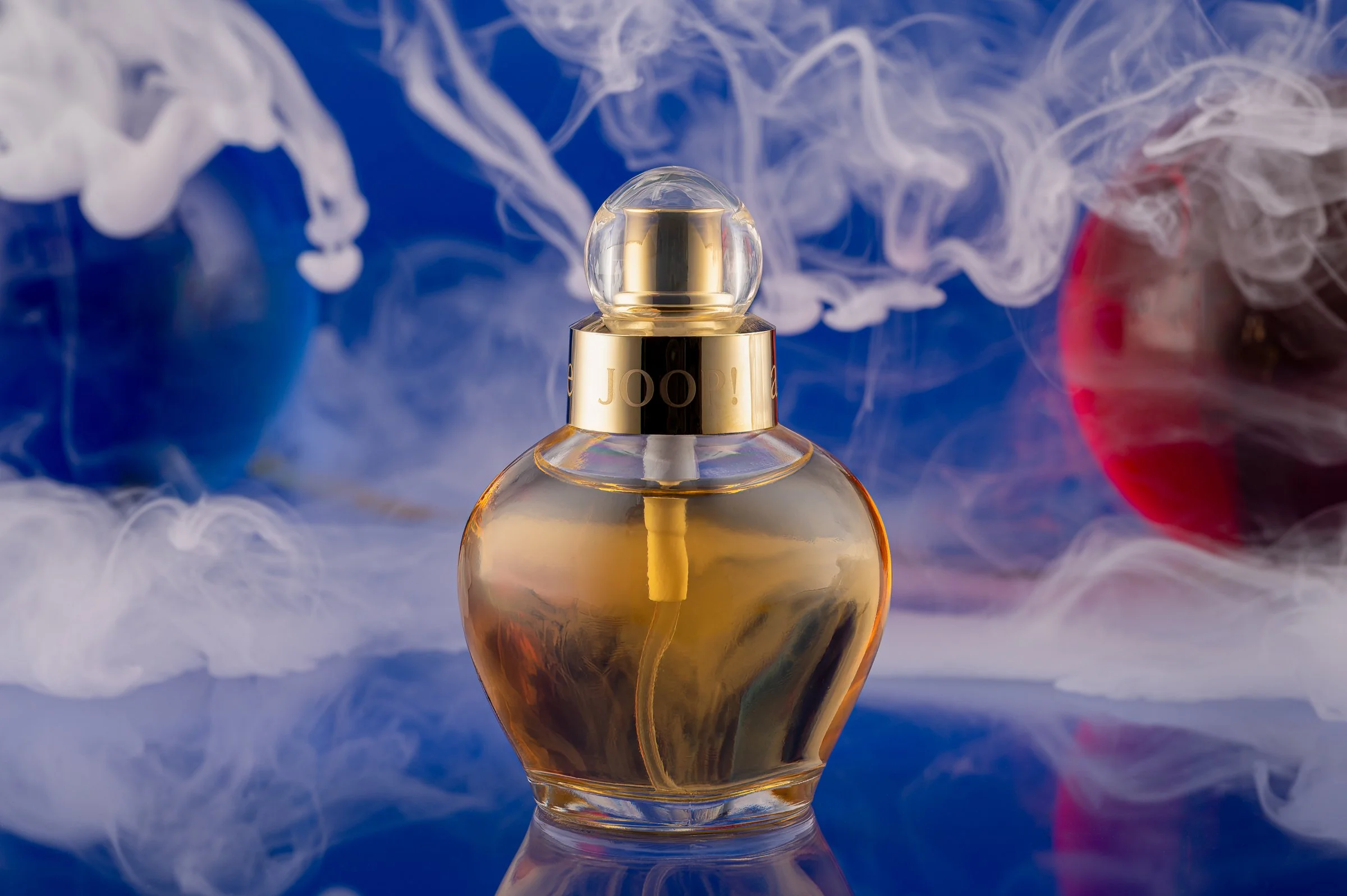 Professionelle Produktfotografie Joop! All About Eve Damenparfüm, atmosphärische Inszenierung mit weißem Nebel und farbigen Akzenten in Blau und Rot, weiche Lichtführung auf dem Glasflakon, technischer Clean-Shot.