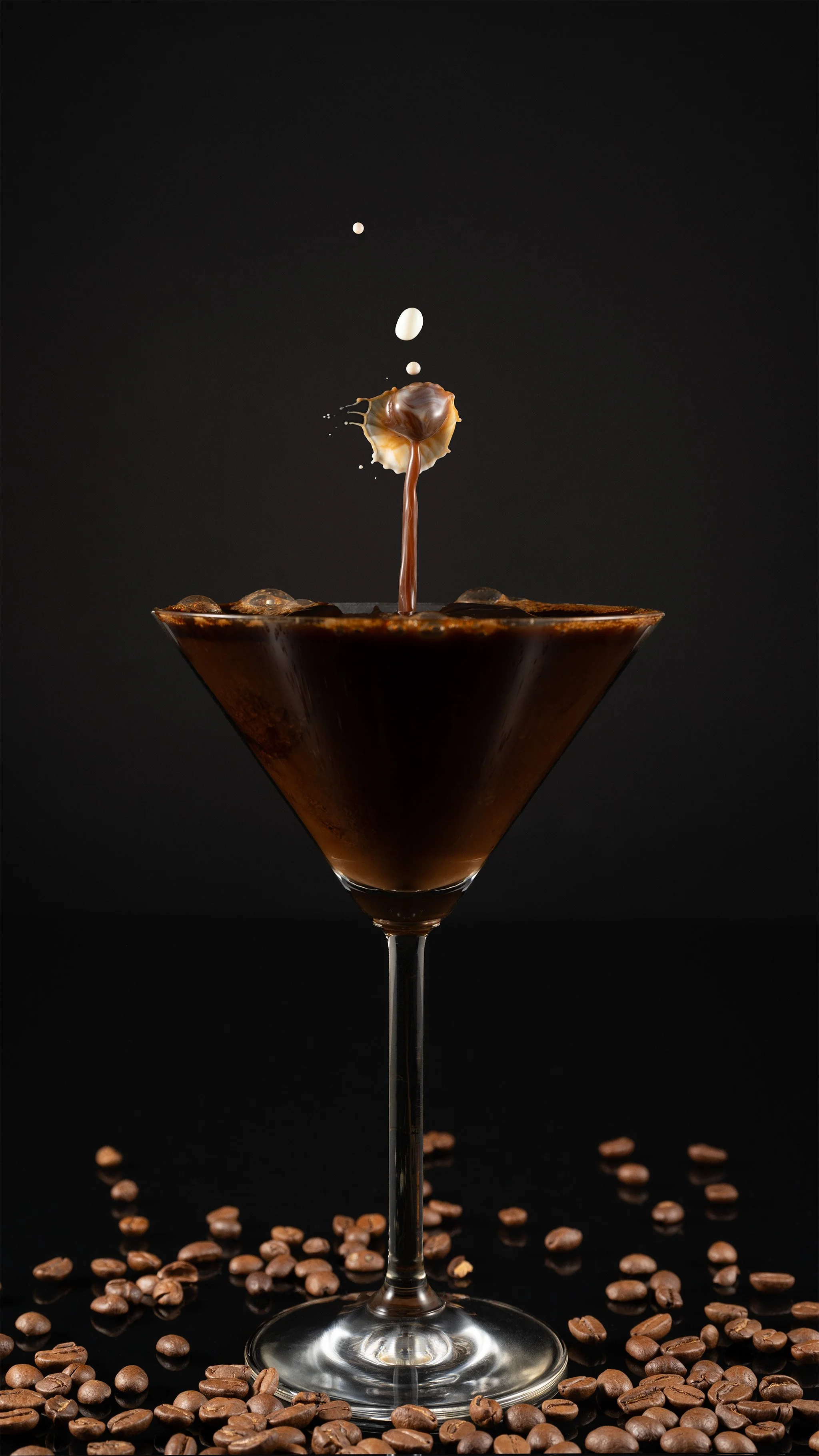 Professionelle Food-Fotografie, Espresso Martini im Kelchglas mit dynamischem Kaffeesplash und Milchtropfen, Dekoration aus Kaffeebohnen auf schwarzem Grund, High-Speed-Fotografie, technischer Clean-Shot.