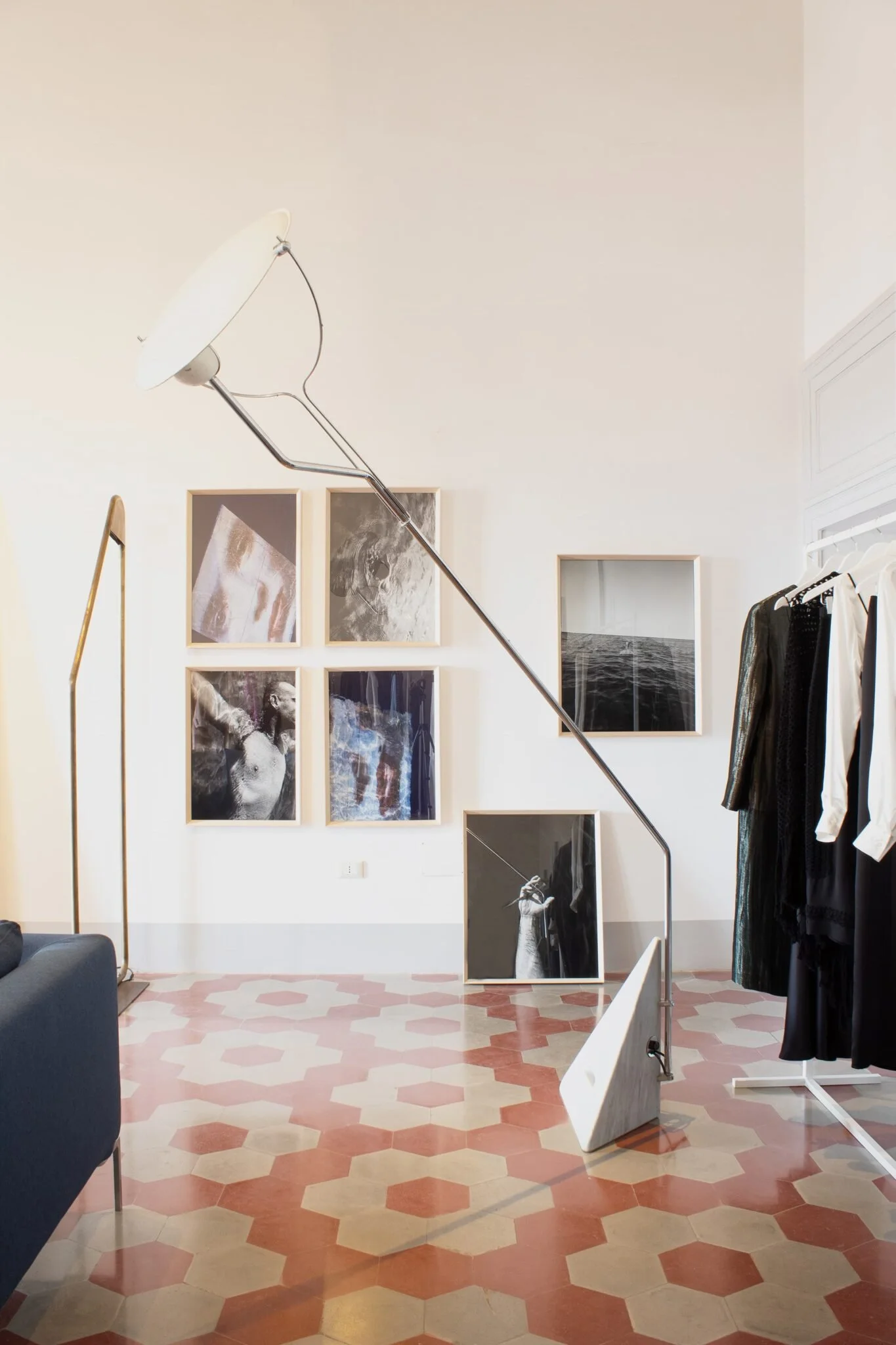 Interno di una galleria d'arte con fotografie in bianco e nero a parete, una sedia bianca e un abbigliamento esposto su una gruccia.