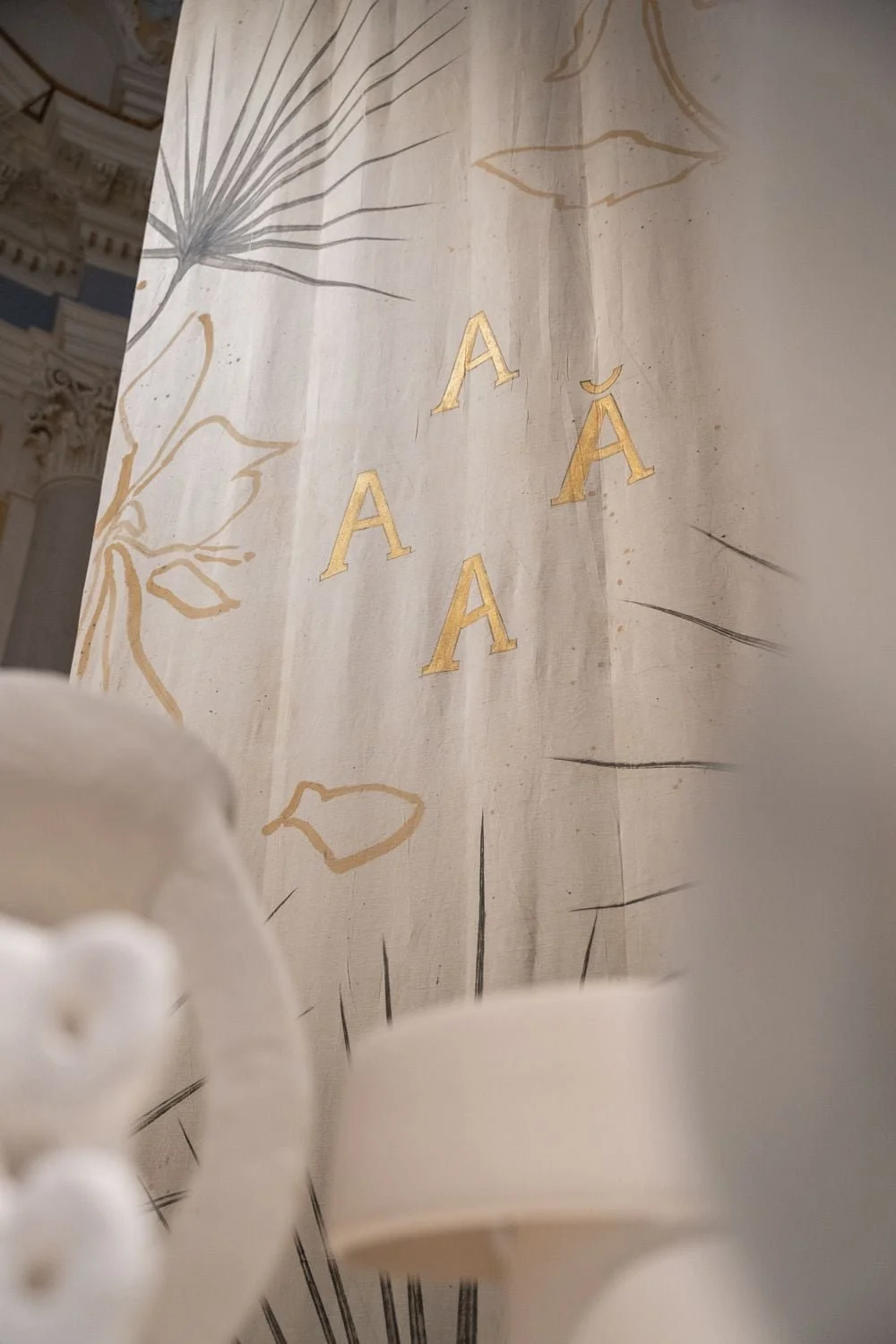 Decorazione con lettera A dorata su sfondo chiaro con disegni floreali.