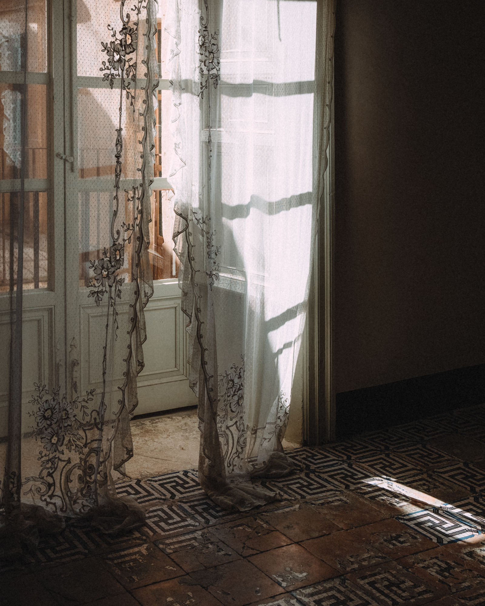 Vetrata con tende di pizzo ricamate che lascia filtrare la luce del sole in una stanza