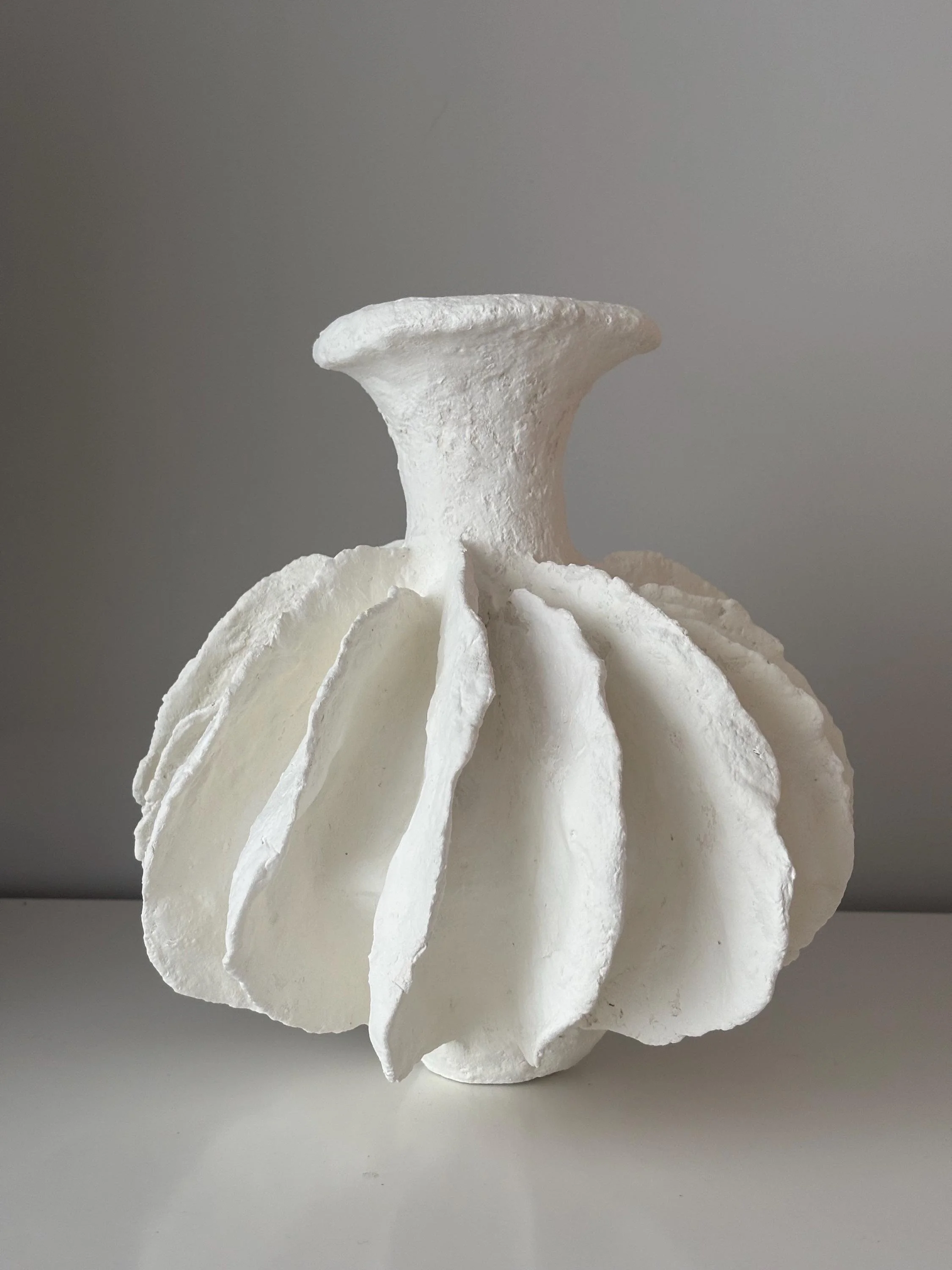Pleated Vase N.28, handmade white pleated paper clay vase, folded form, in a room setting. Papier Atelier London