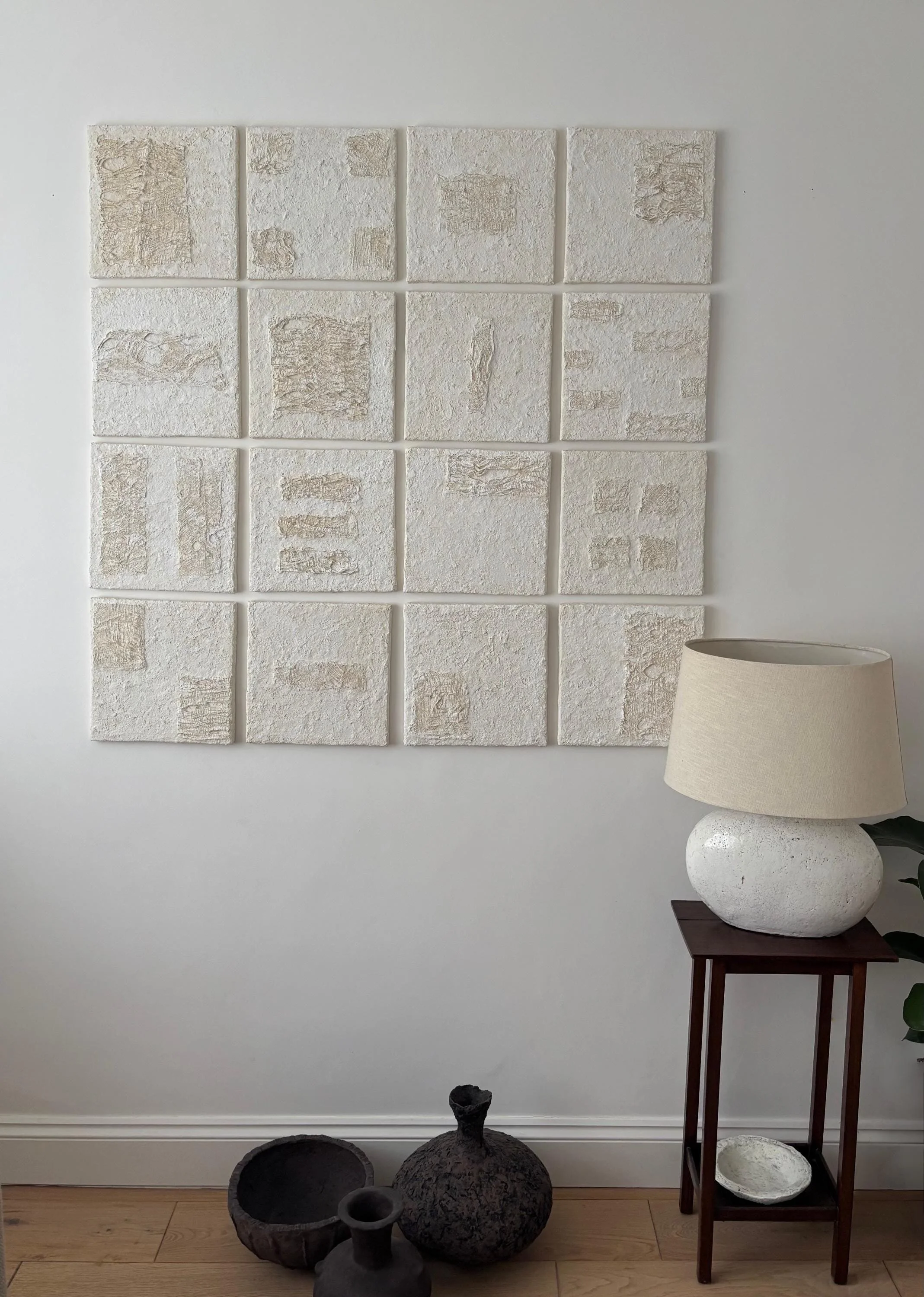 Wall Set N.35, handmade set of sixteen paper clay wall pieces, textured canvases, in a room setting. Papier Atelier London