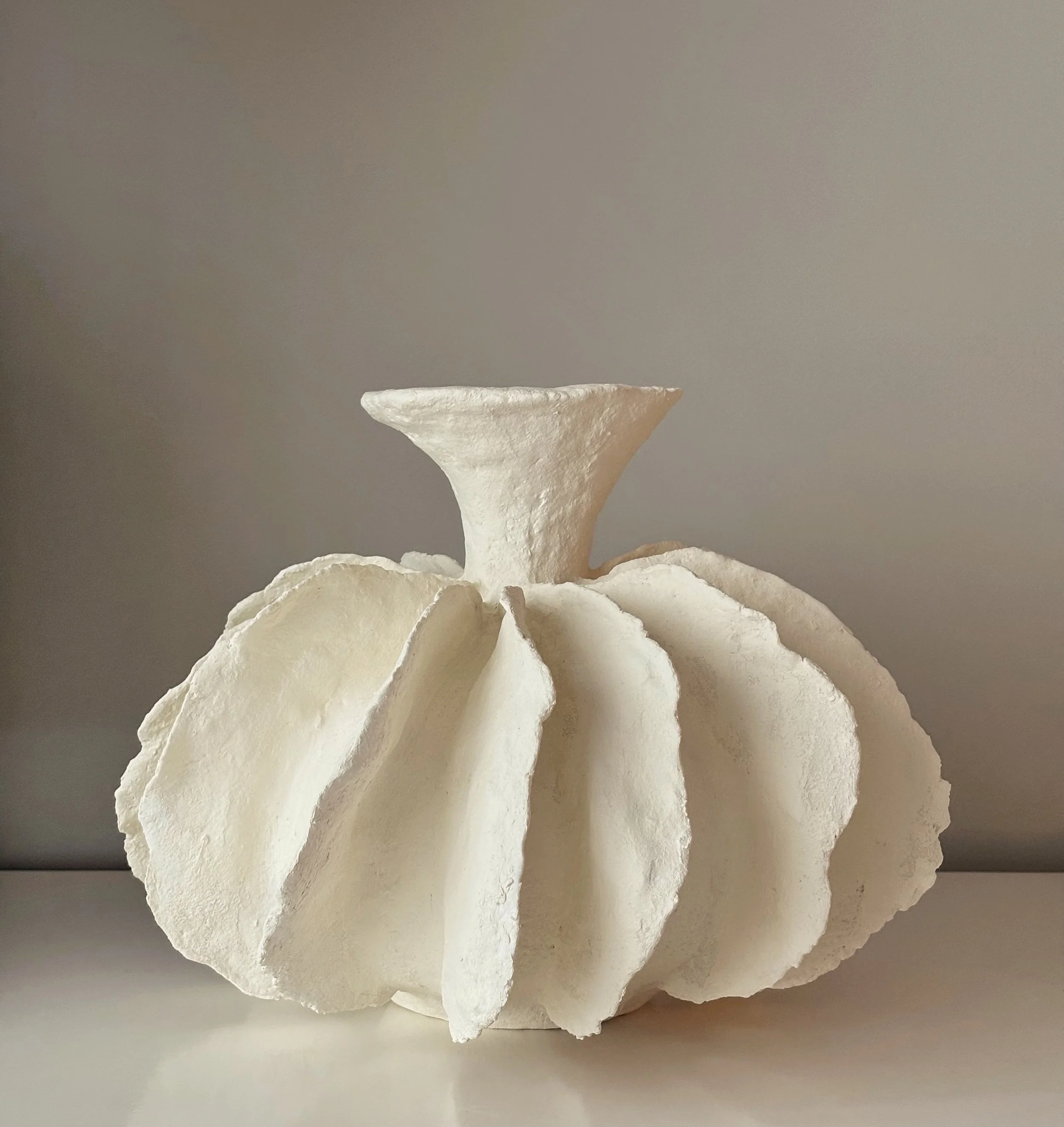 A sculptural white vessel with dramatic pleated folds and a narrow flared neck.