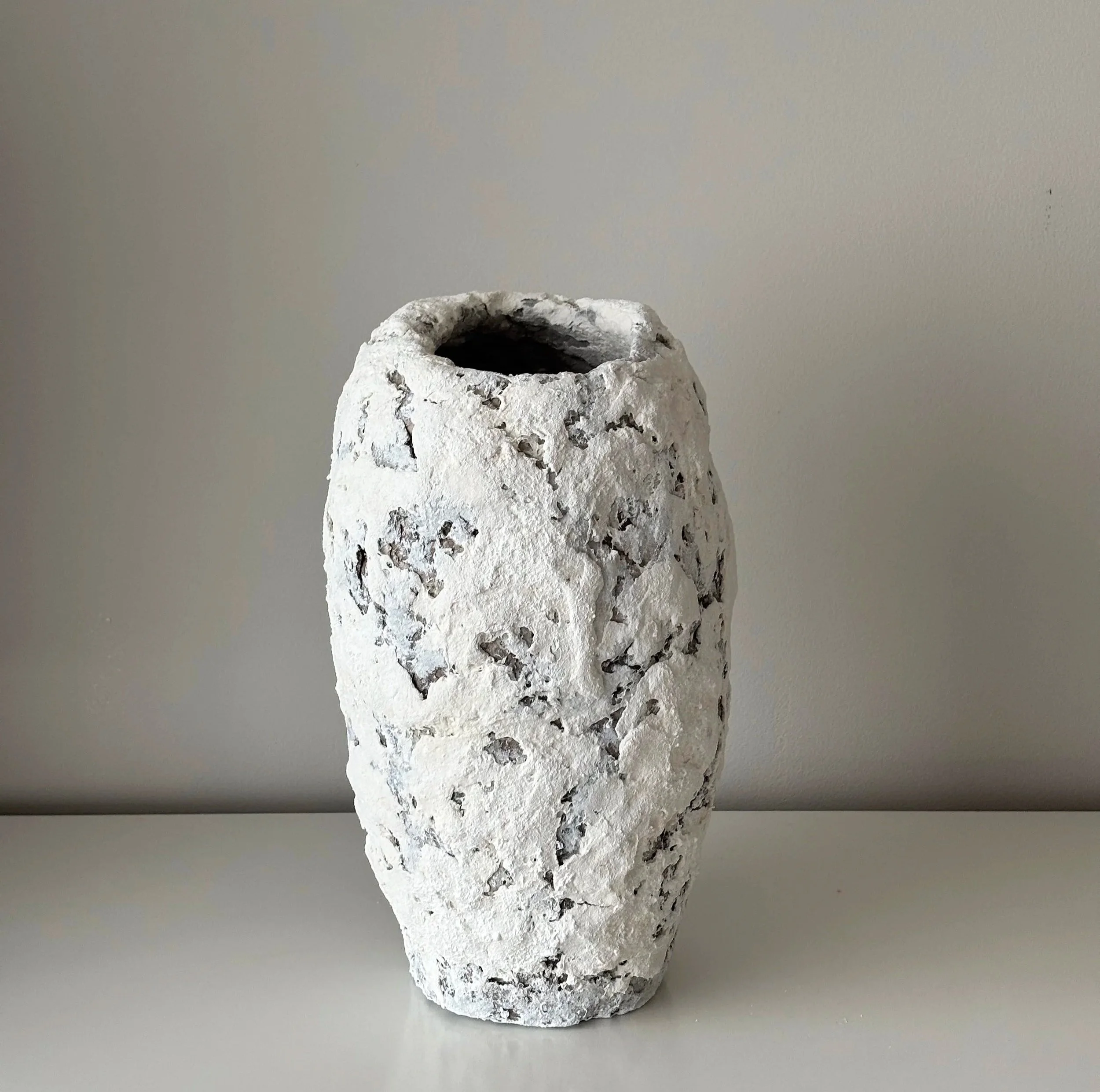 A tall, cylindrical form in white with a deeply textured, crater-like surface and irregular opening. The organic exterior evolved naturally during the making process.