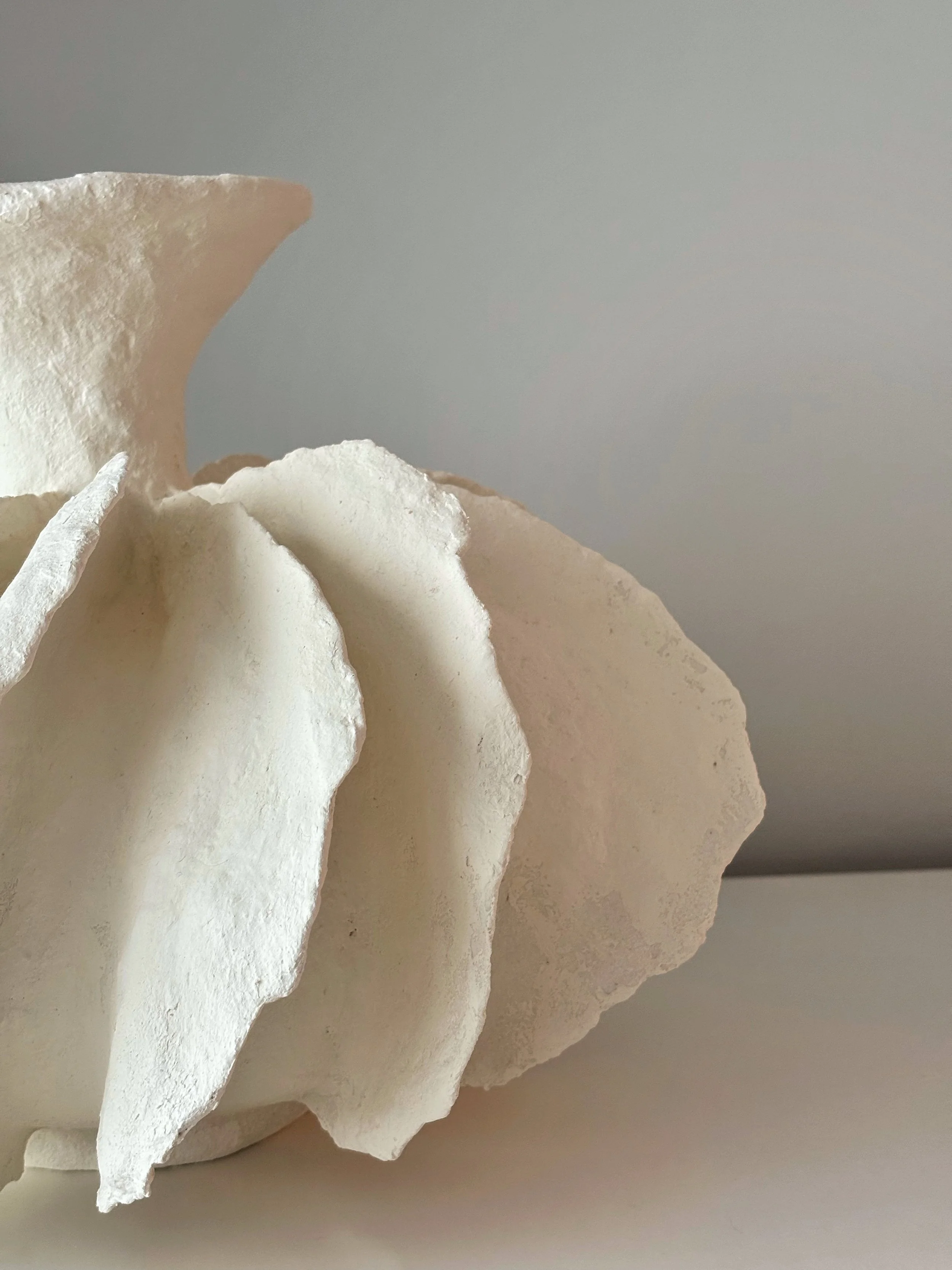 White Pleated Sculpture Vase N.12, white paper clay vase viewed from an alternate angle highlighting asymmetrical shape, from Papier Atelier London