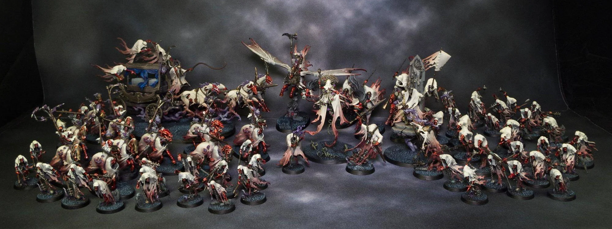 Miniature fantasy battle scene with numerous figures, including soldiers and a central character wielding a sword, set against a dark background with dramatic clouds.