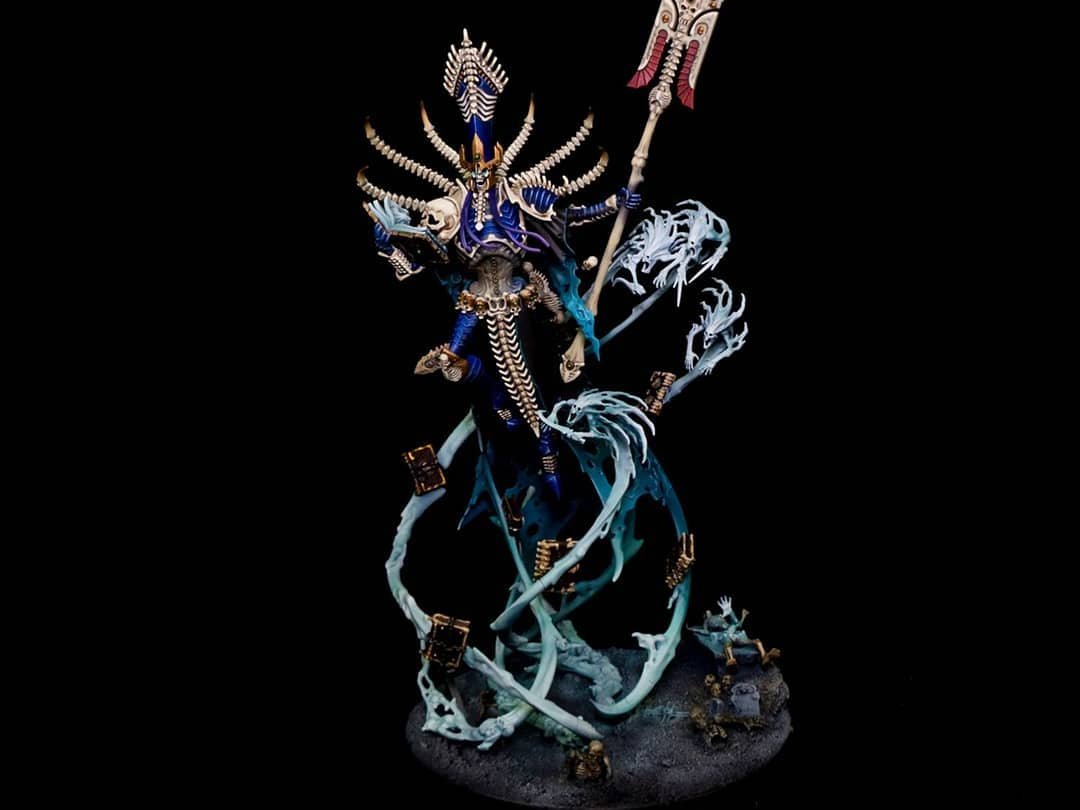A detailed fantasy miniature figure of a sorcerer or warrior with a staff, adorned in blue and white armor, surrounded by swirling mist and small skulls, set against a black background.