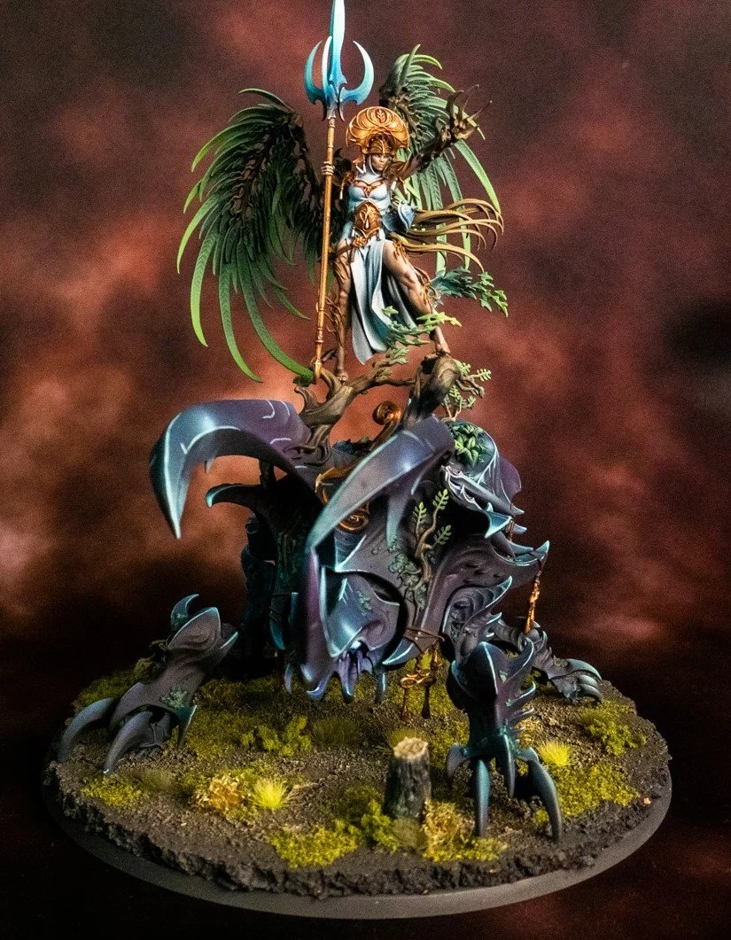 Miniature fantasy figure of a winged warrior woman with a trident, standing on a large, armored insect-like creature with multiple legs, on a detailed base with moss and small plants.