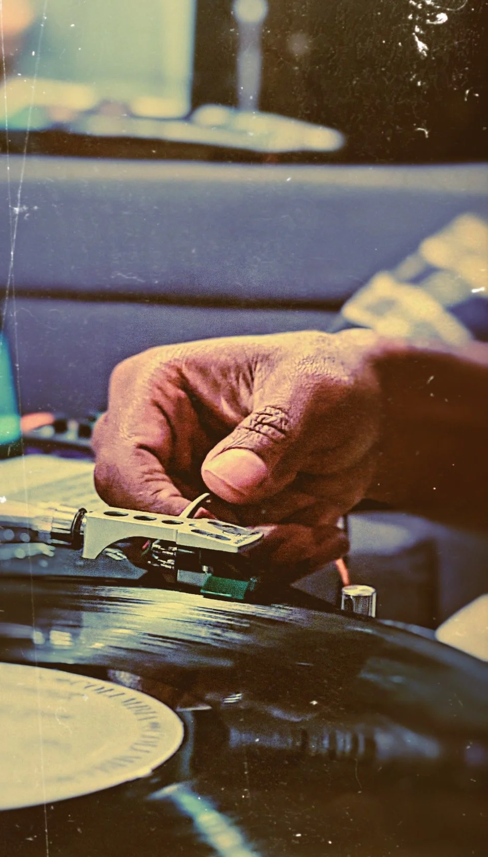 Close-up of a hand adjusting the tonearm on a turntable, with a vinyl record spinning underneath.