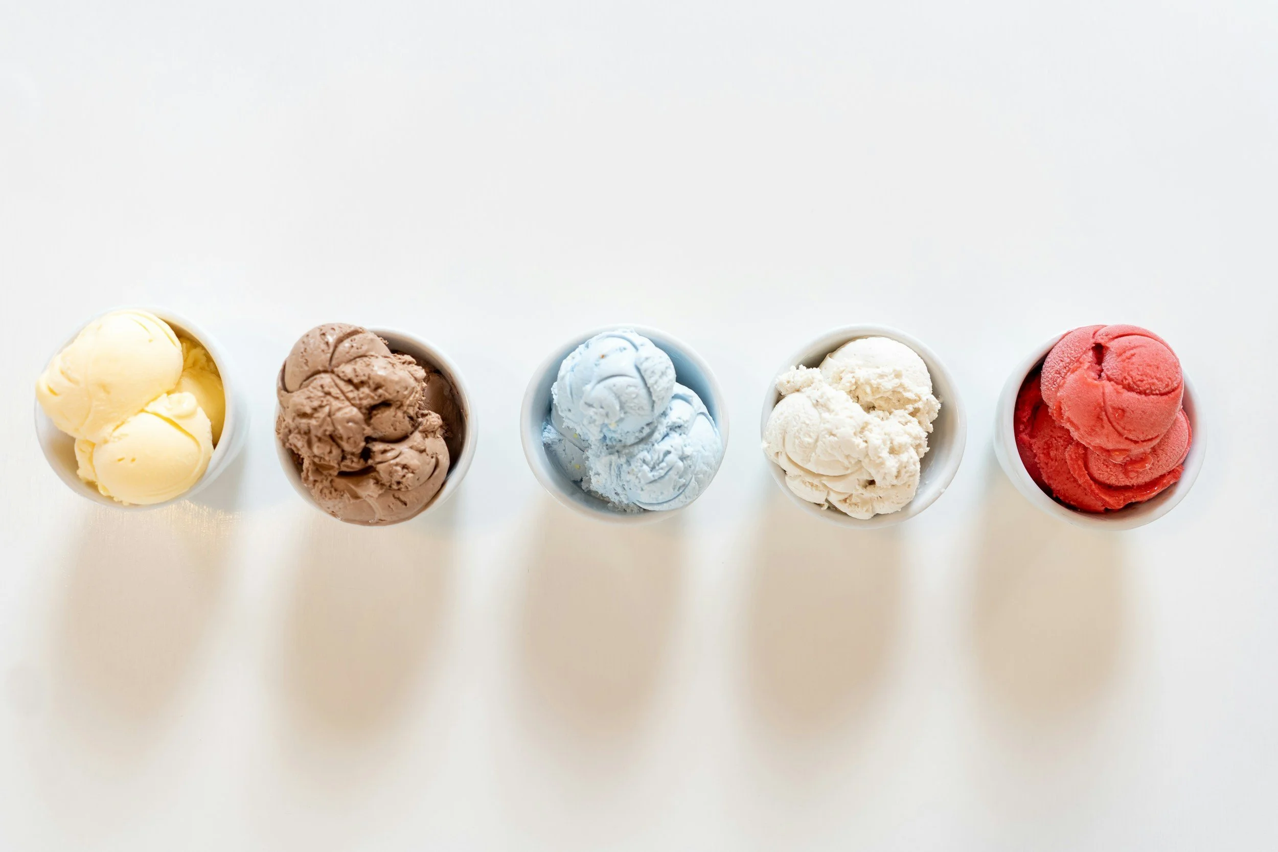Five cups of different flavors of ice cream arranged in a row on a white surface.