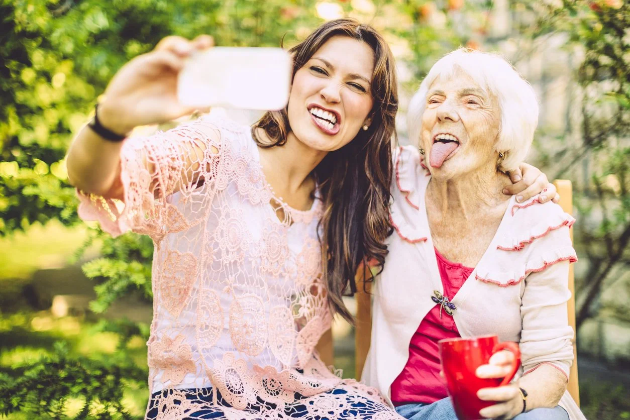 Young woman and older woman laughing and taking a selfie together outdoors