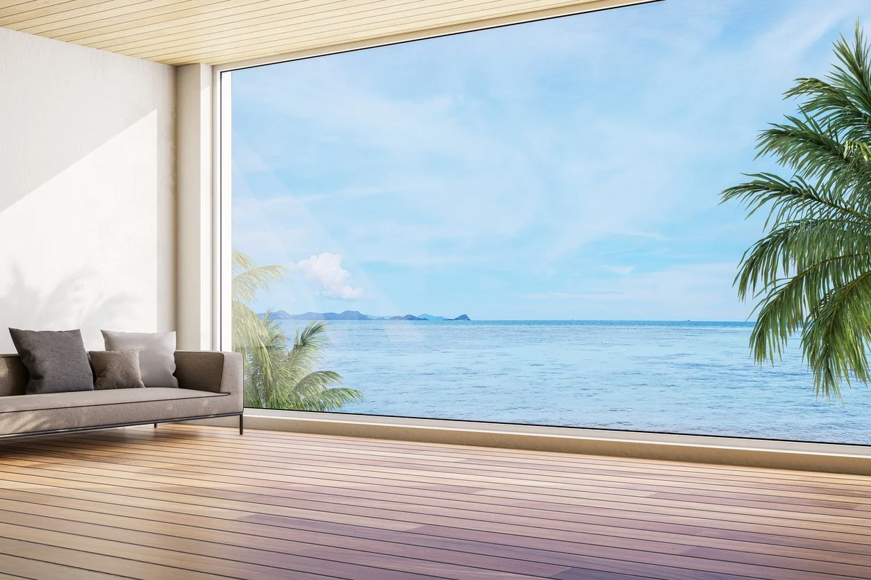 Bright modern living space with floor-to-ceiling window overlooking a calm ocean and palm trees