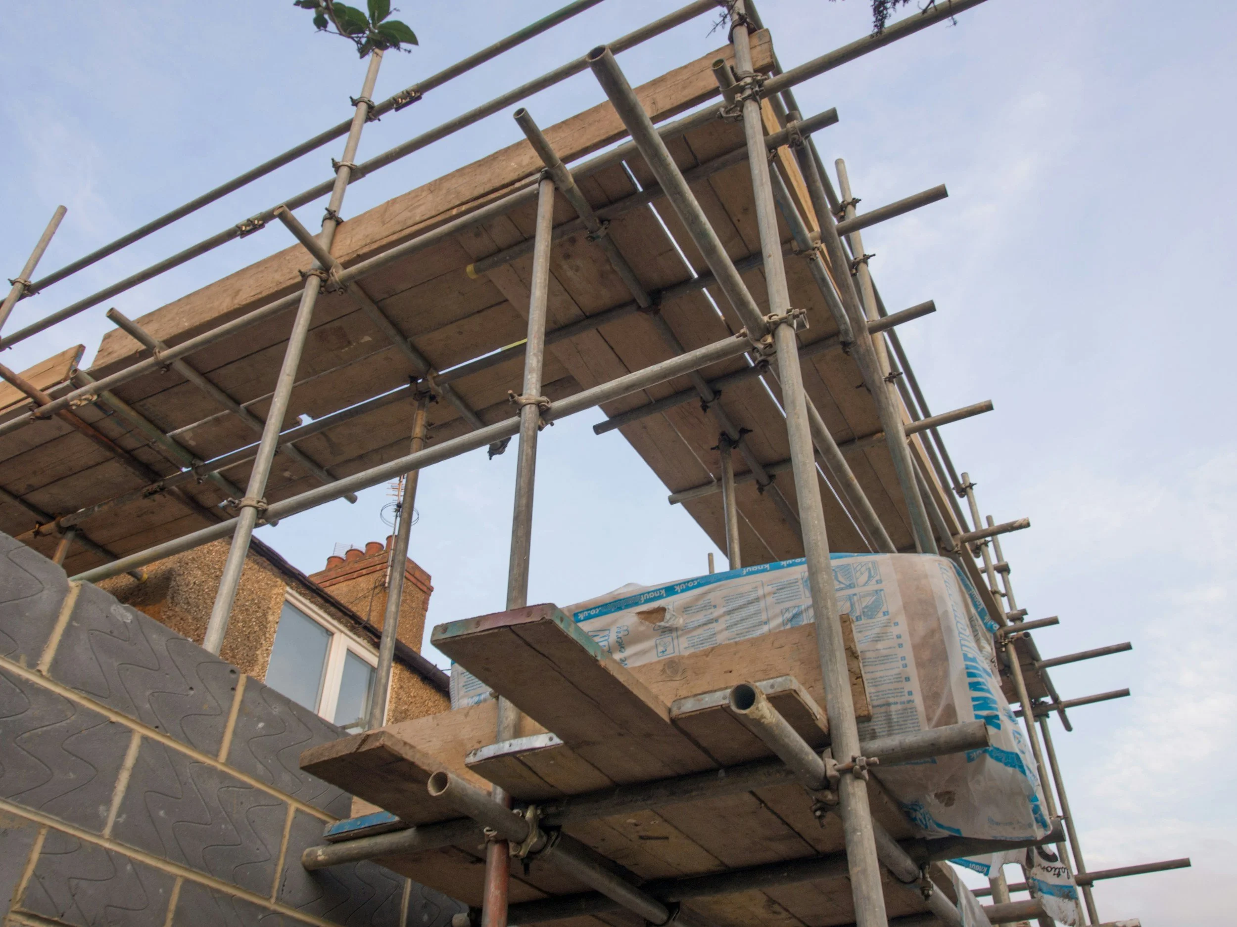 View of construction scaffolding set up on a building exterior, with wooden planks on the scaffolding and a blue sky in the background.
