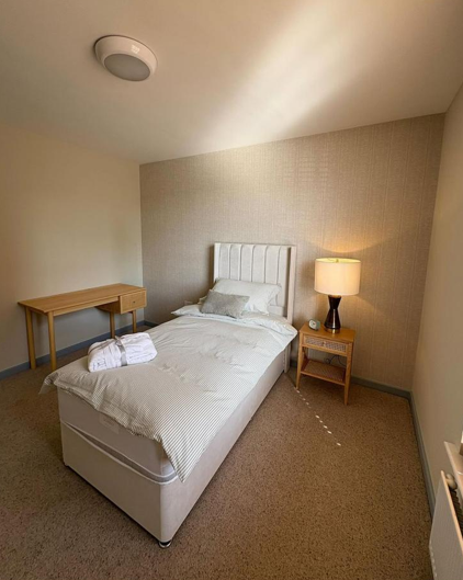 Single hotel room with a bed, bedside table with lamp, and a small wooden table in the corner.