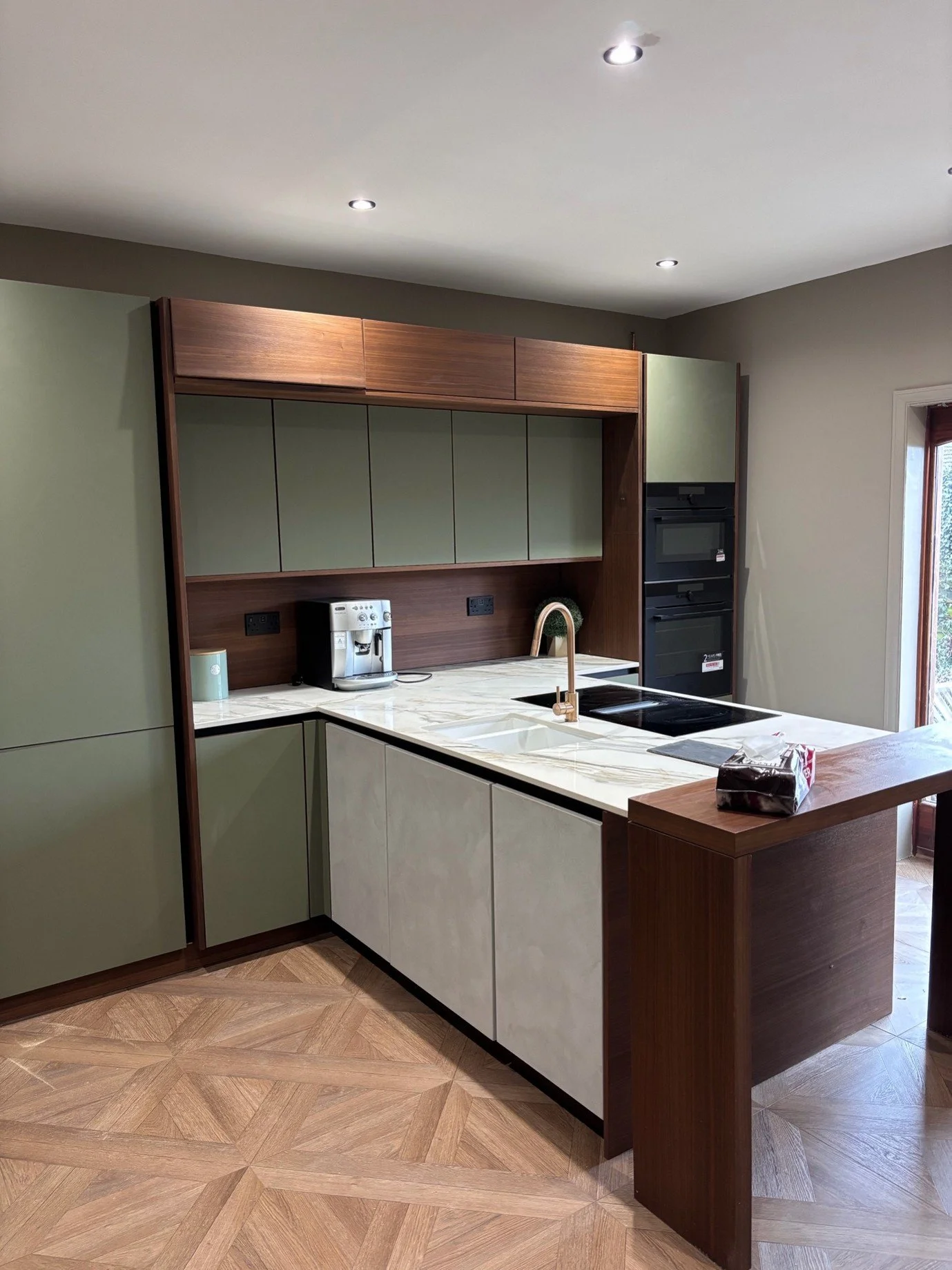 Modern kitchen with wooden and green cabinets, marble countertop, and built-in appliances.