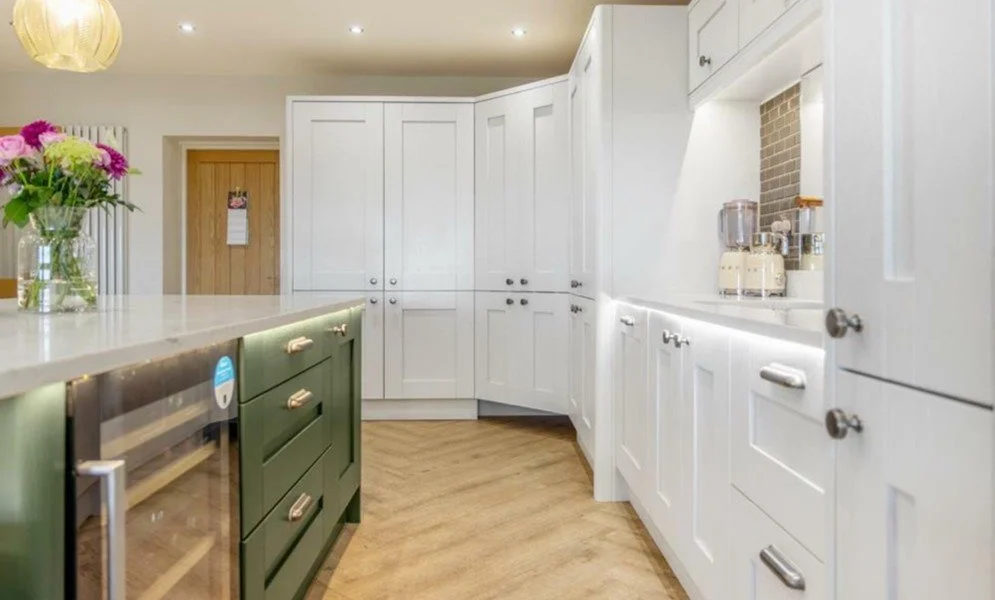 Modern kitchen with white cabinets, a green kitchen island, and a bouquet of pink and green flowers on the countertop.