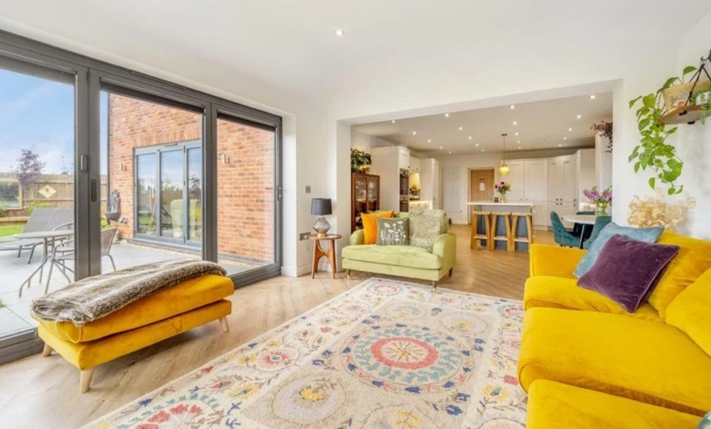 Bright living room with large sliding glass doors opening to a patio, with colorful sofas and a patterned rug.