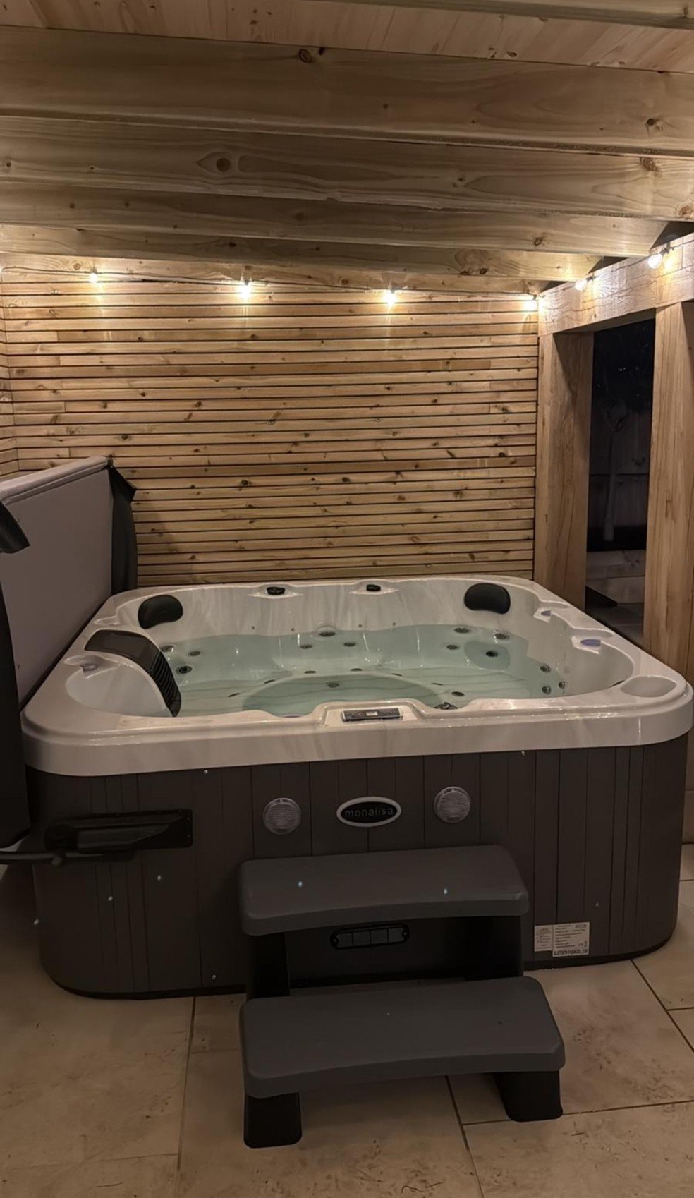 Indoor hot tub with a wooden wall and ceiling, string lights, and a staircase to the right.