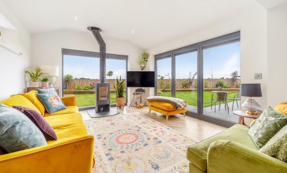 Living room with large sliding glass doors, yellow and green sofas, a rug, a modern black fireplace, and outdoor patio furniture.