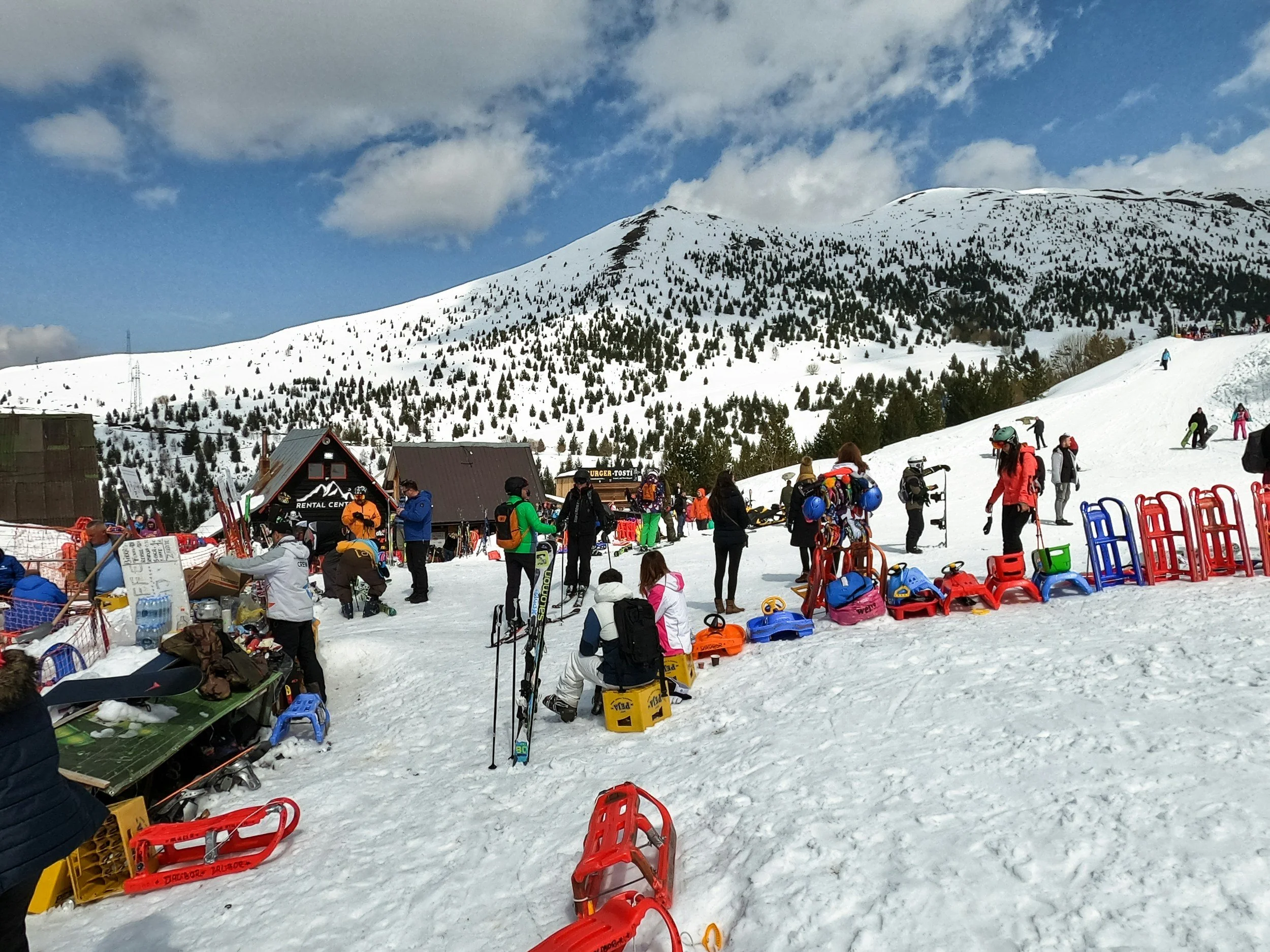 Snowy mountain resort with skiers and snowboarders, colorful equipment, and a rental shop in the background.
