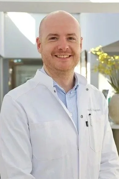 Mann in weißem Arztkittel im Krankenhaus, lächelnd.