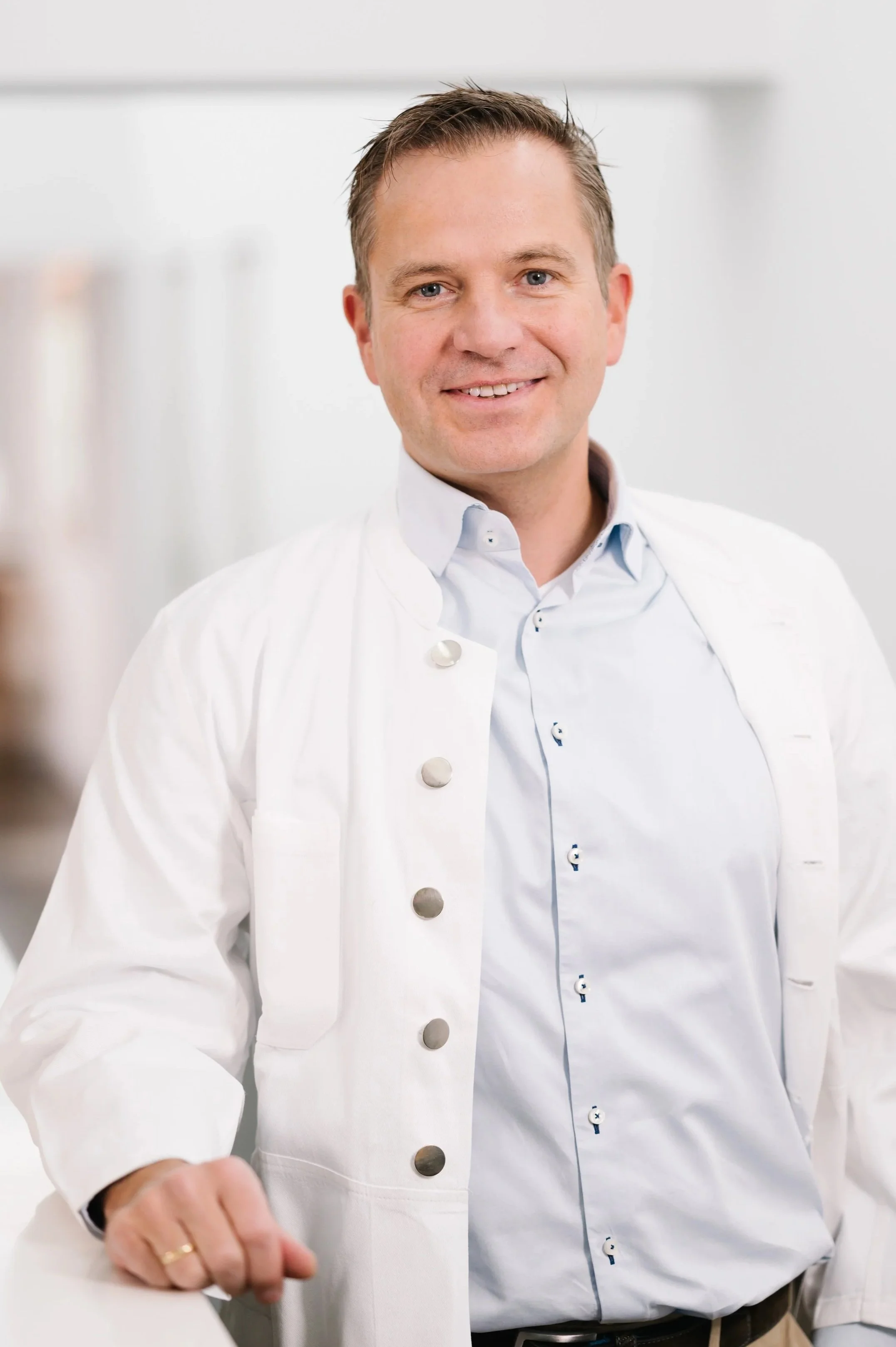 Ein Mann in weißem Arztkittel lächelt in die Kamera.