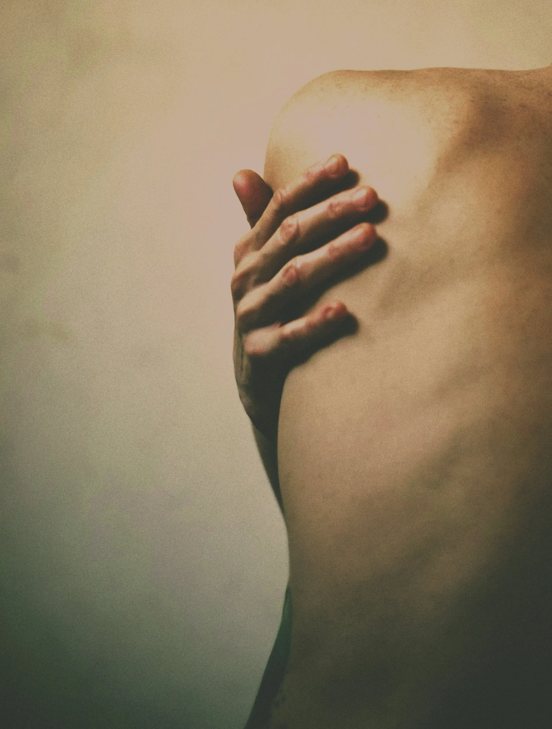 A person with a bare shoulder and back, holding their shoulder with their hand.