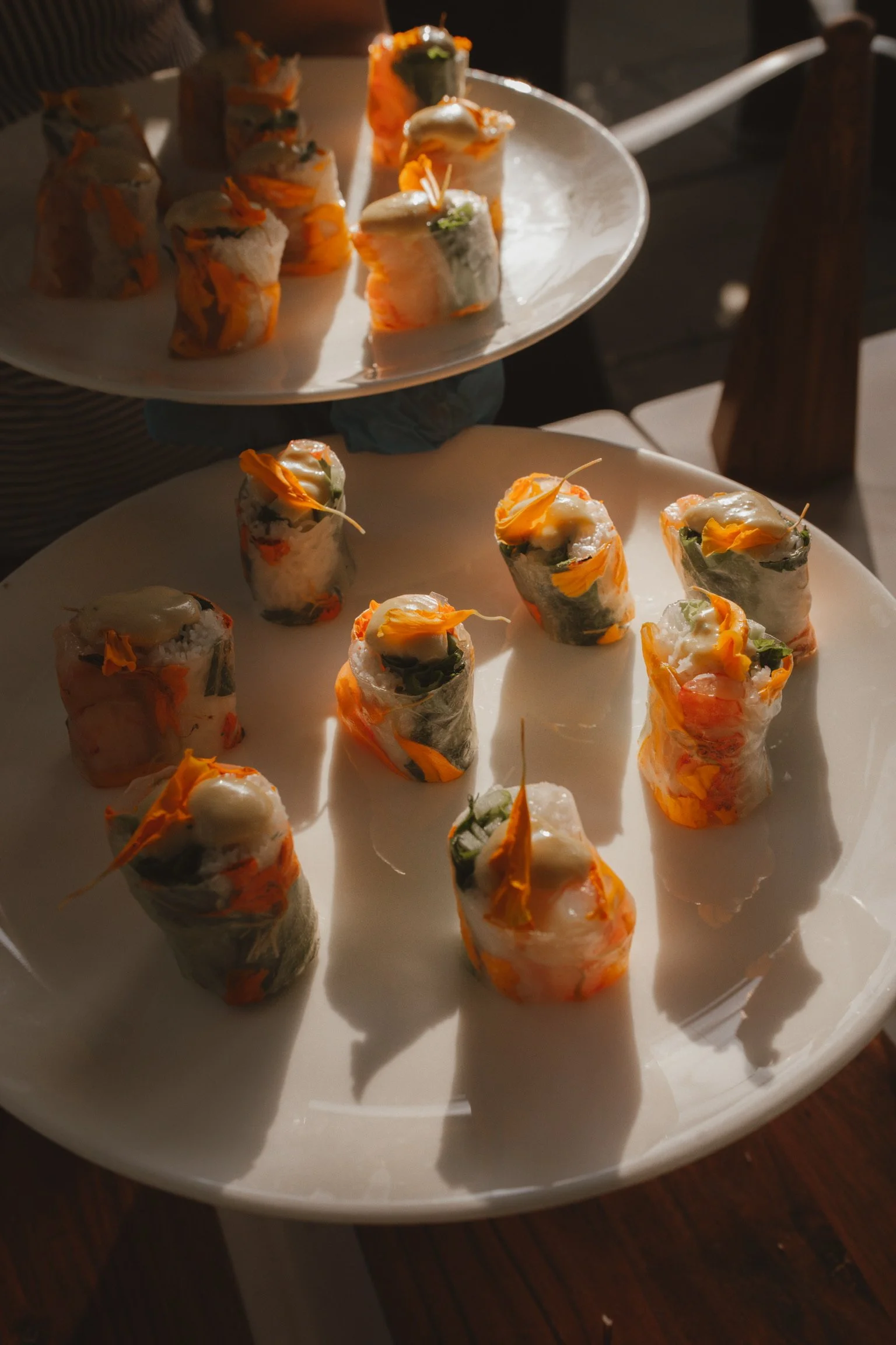 Plate of assorted sushi rolls with various ingredients, garnished with edible flowers, served on white plates.