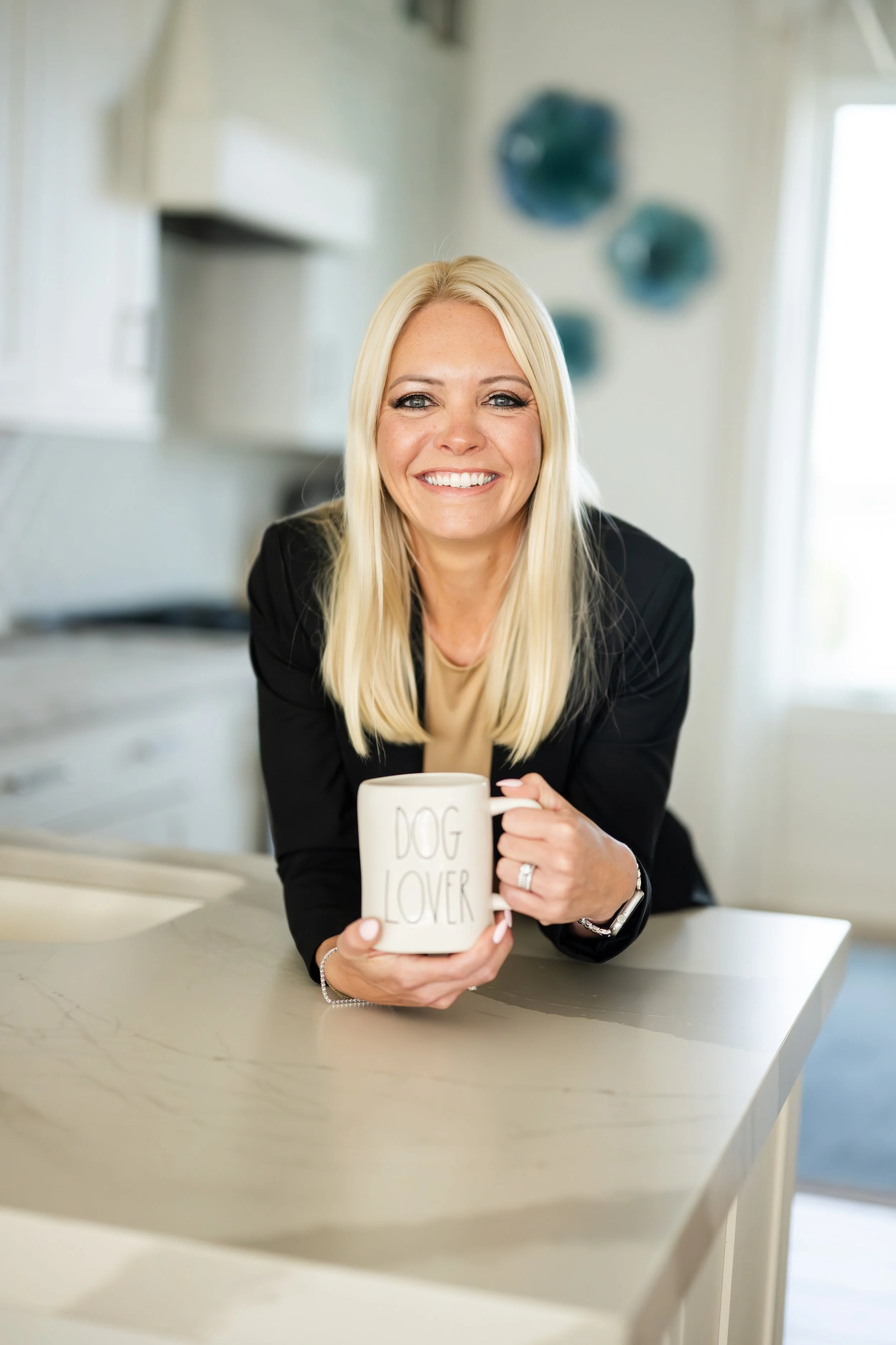 Lori Roland, broker and founder of Golden Coast Real Estate, holding a white mug that says 'Dog Lover' in a bright kitchen.