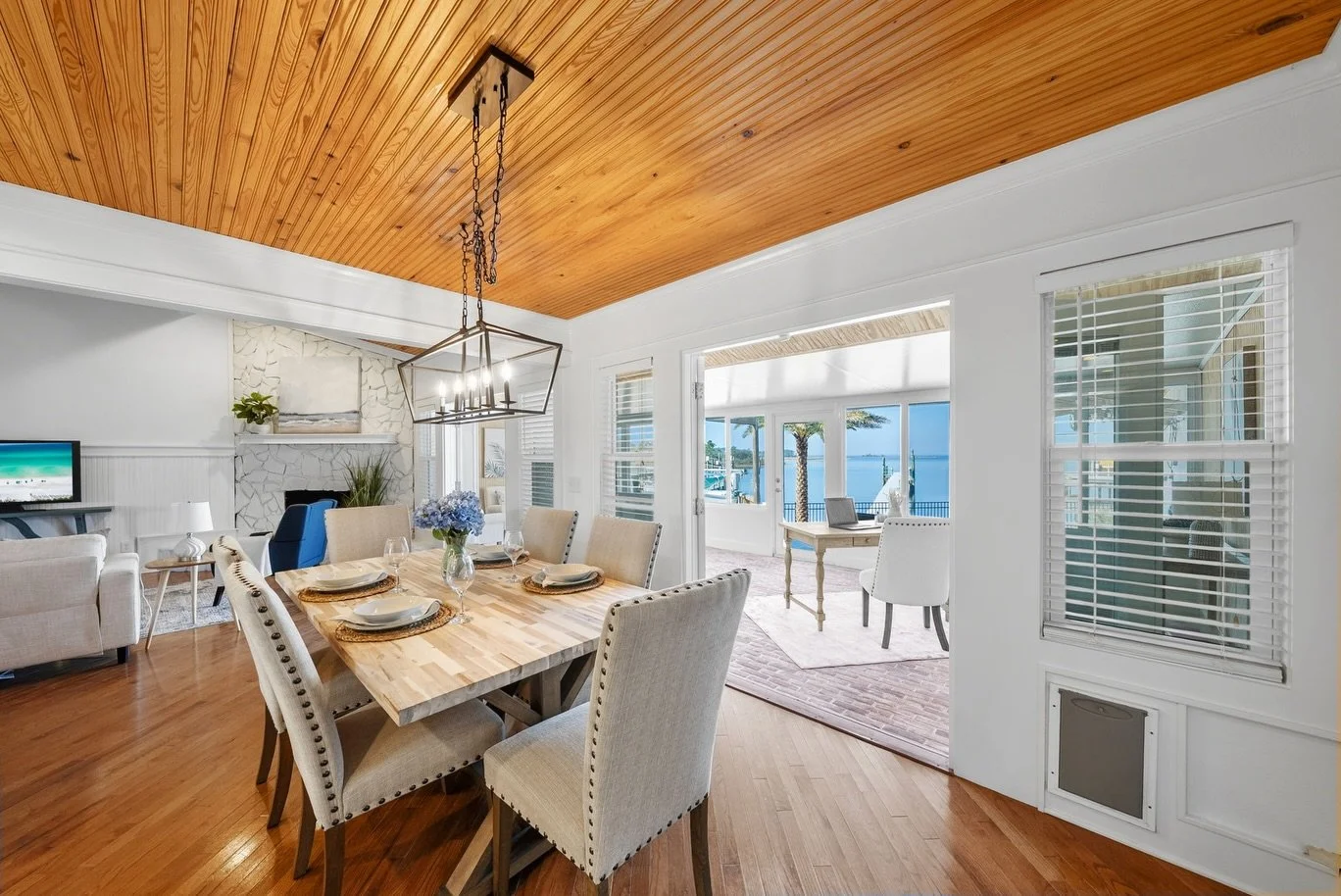 Emerald Coast Staging featured dining room with wooden table set for four, overlooking a waterfront view through sliding glass doors, with a white and wood-themed interior.