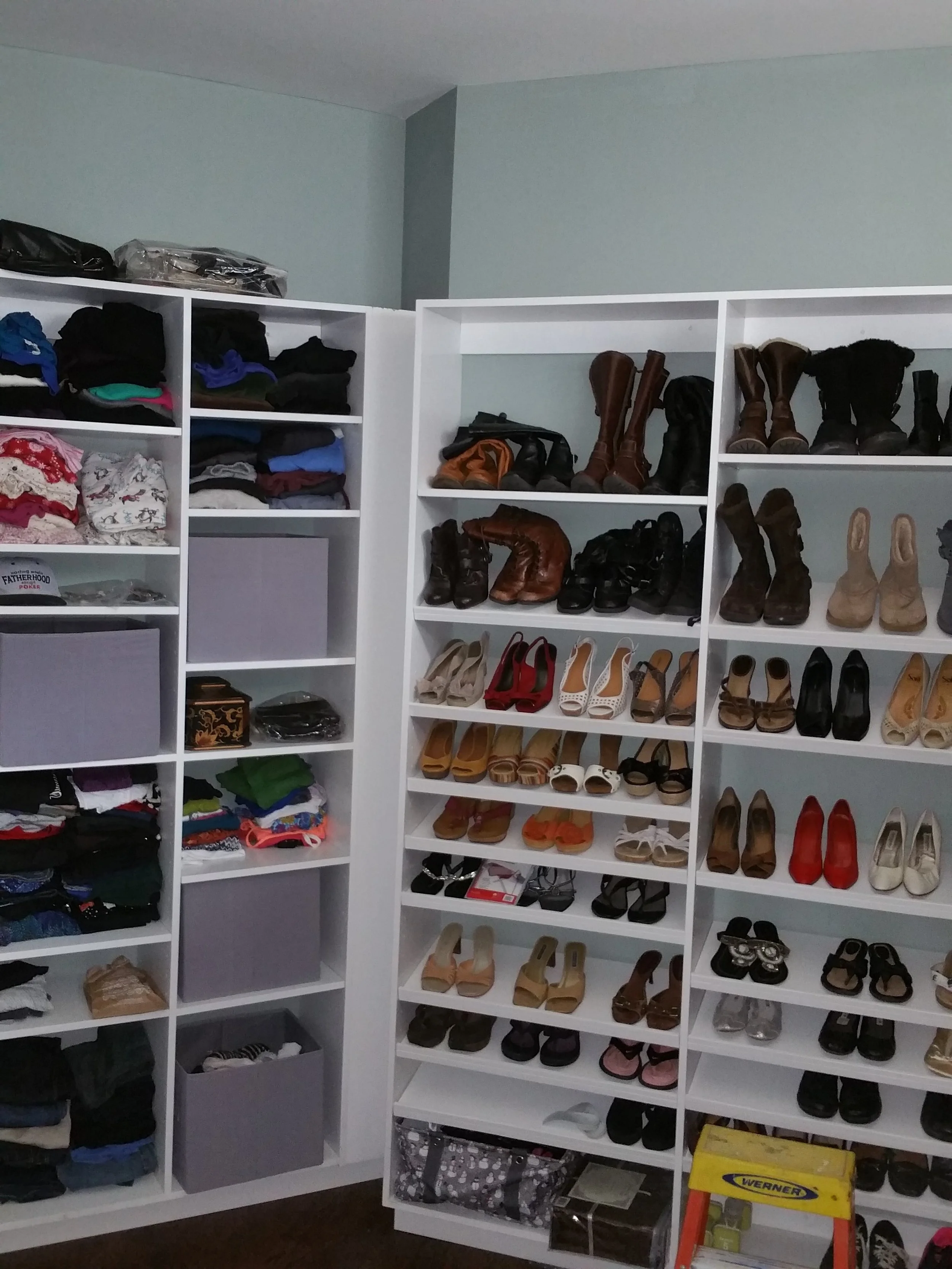 White shelving units filled with folded clothes, shoes, and accessories in a closet or storage room.