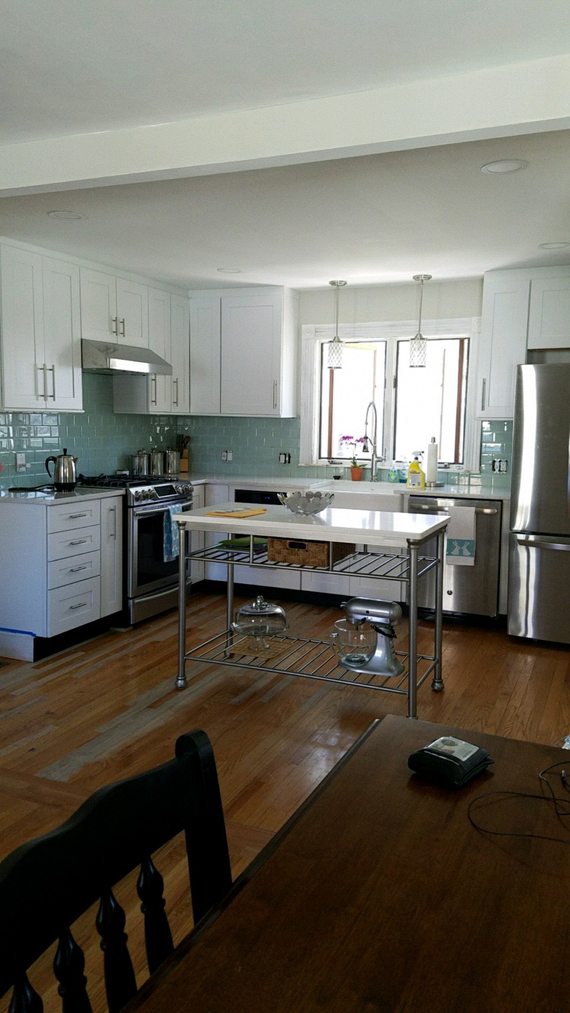 A bright kitchen with white cabinets, stainless steel appliances, a kitchen island with a metal rack, and hardwood floors.