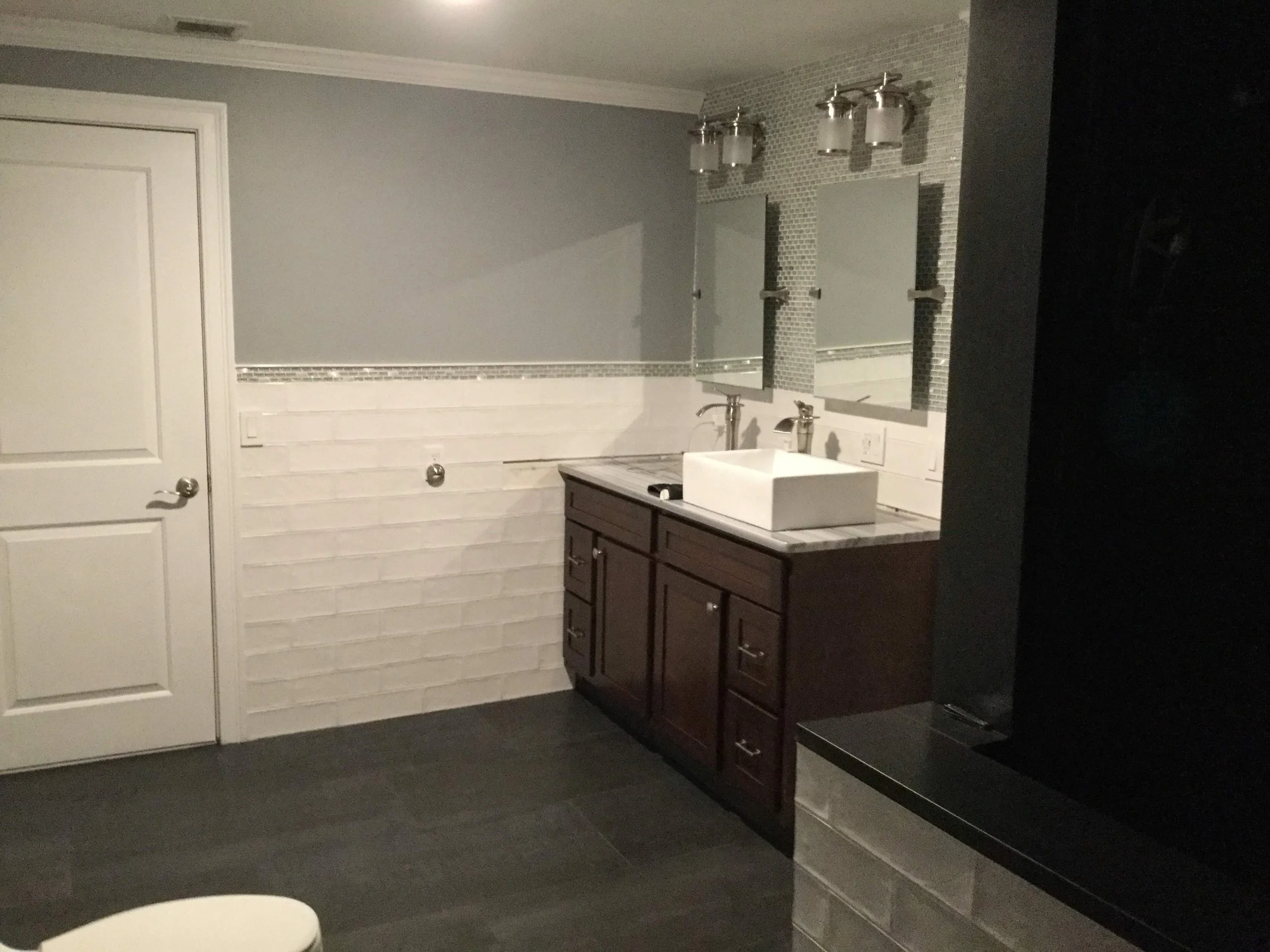 Bathroom with a dark wood vanity, a vessel sink, two mirrors, and three light fixtures. The wall features white brick and gray paint.