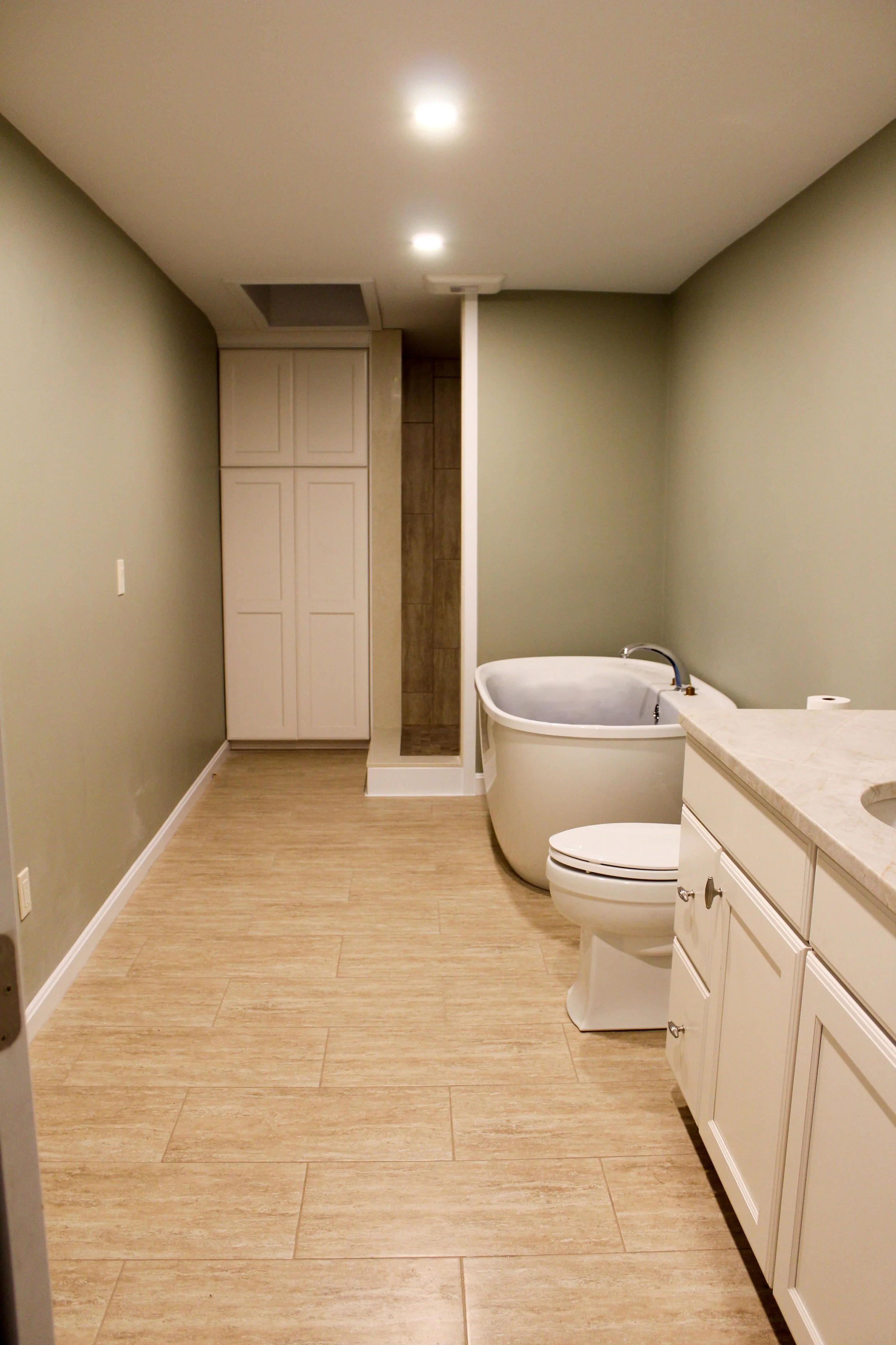 Modern bathroom with wood-look tile flooring, a bathtub, toilet, and vanity with a sink, illuminated by recessed ceiling lights.