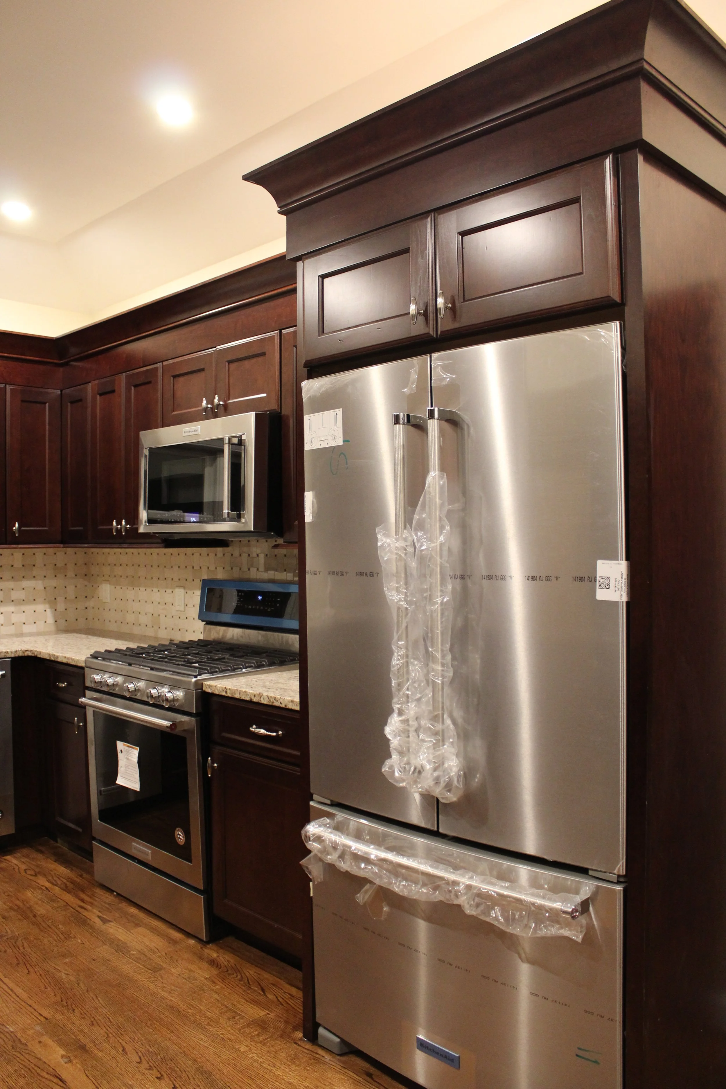 New stainless steel refrigerator in a kitchen with dark wood cabinets and a granite countertop.