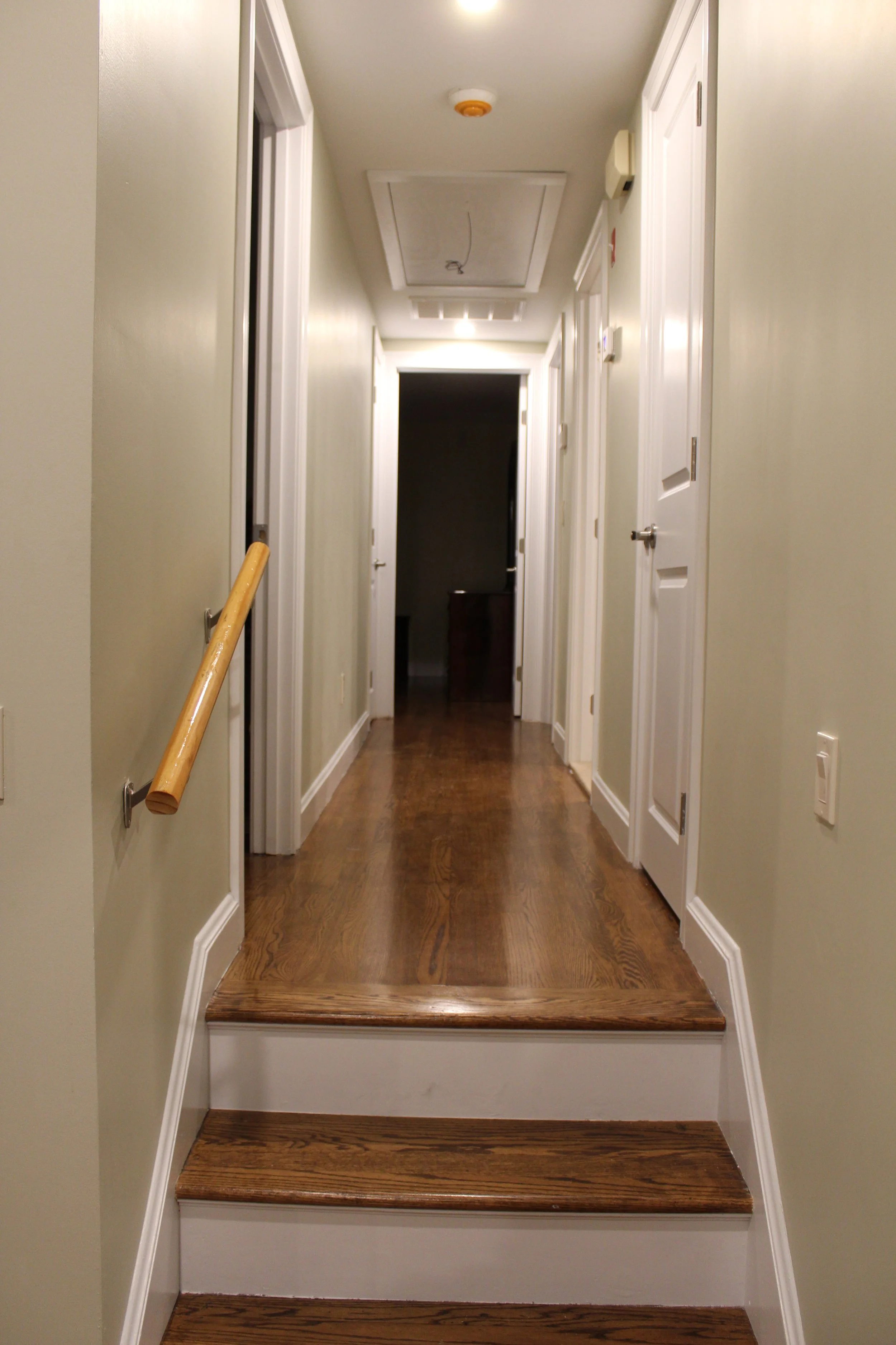 Hallway with wooden stairs, light-colored walls, white doors, and a door at the end of the hallway.
