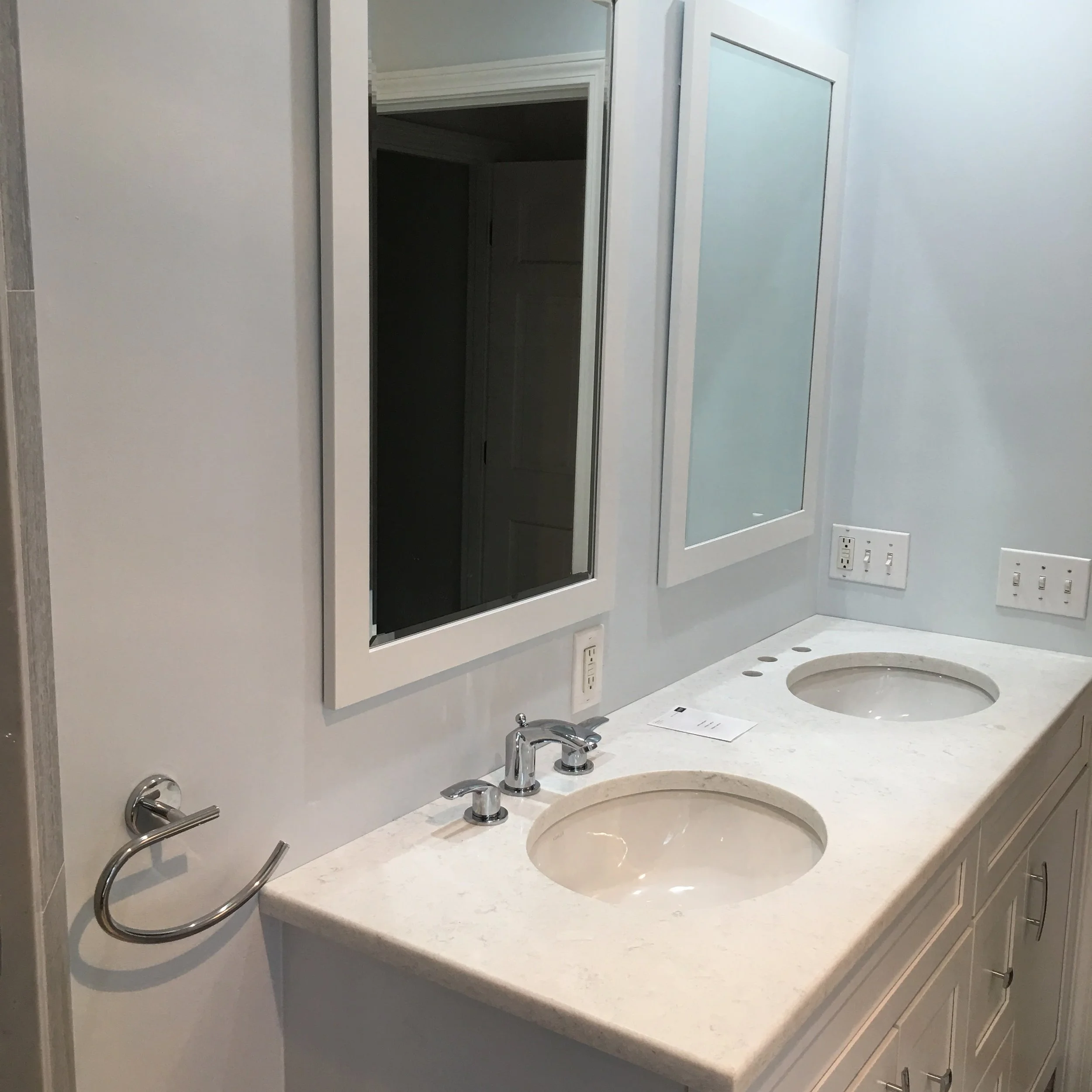 Bathroom vanity with a marble countertop, two oval sinks, mirrors and three electrical outlets.
