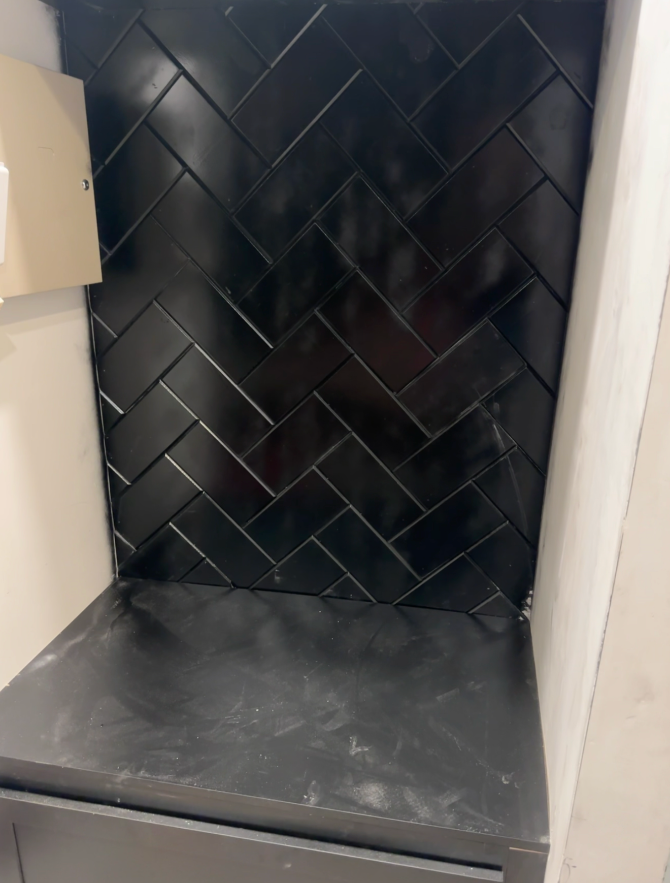 Black herringbone tile wall behind a black countertop in a room corner.