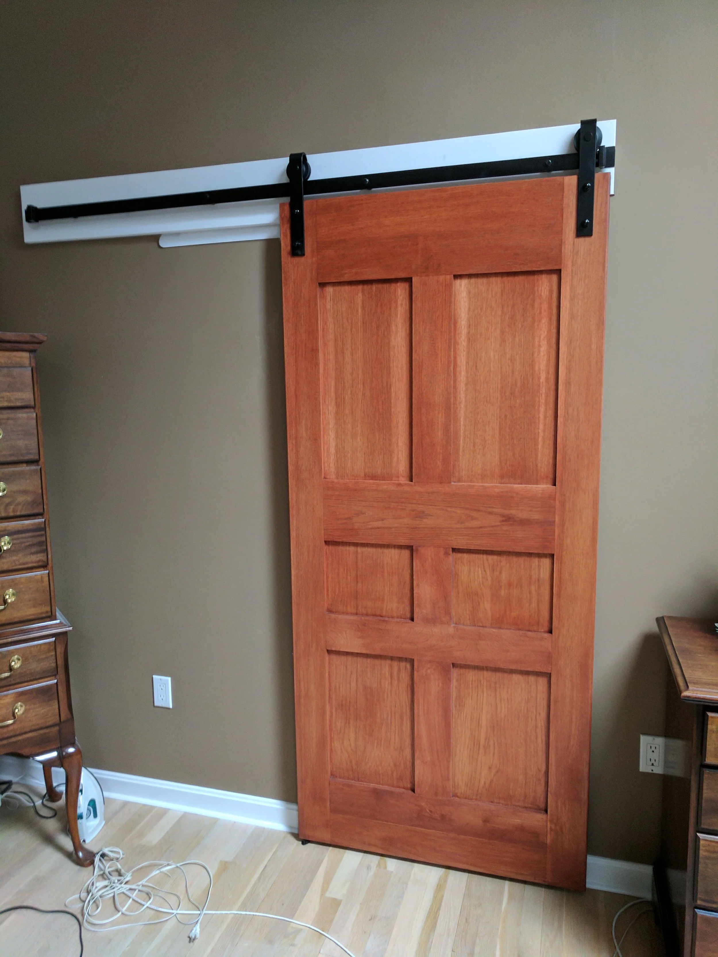 Wooden sliding barn door installed on a sliding rail system in a room with brown walls and light wood flooring.