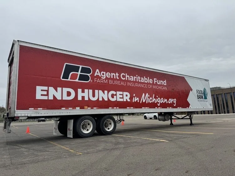 A large semi-truck trailer parked in an empty lot with promotional graphics for a food bank and hunger relief campaign in Michigan.